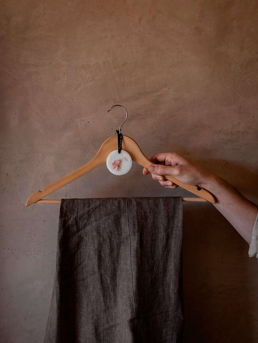 Person holding a wooden hanger with dark pants against a plain wall