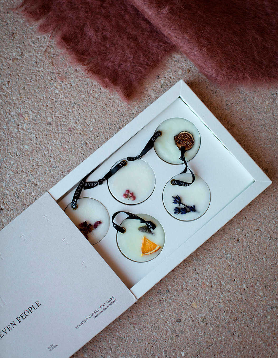 Set of four round ceramic items with floral designs in a box on a textured surface.