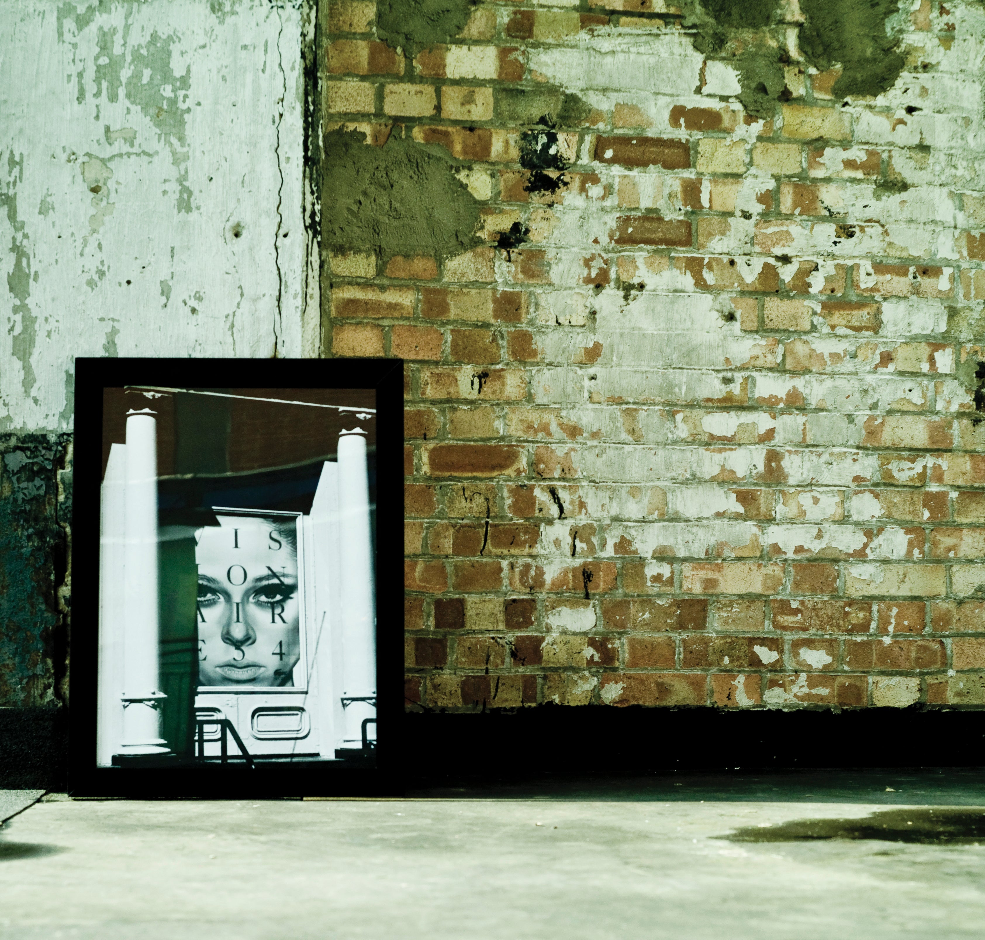 Framed artwork leaning against a textured brick wall.