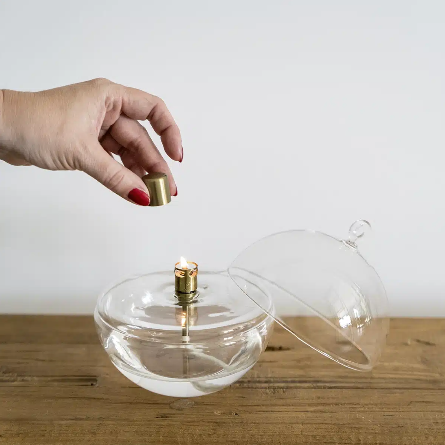 Clear glass container with a gold cap on a wooden surface, hand holding the cap.