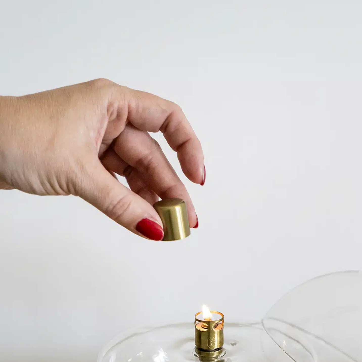 Hand holding a brass lighter above a small candle inside a glass container on a white background