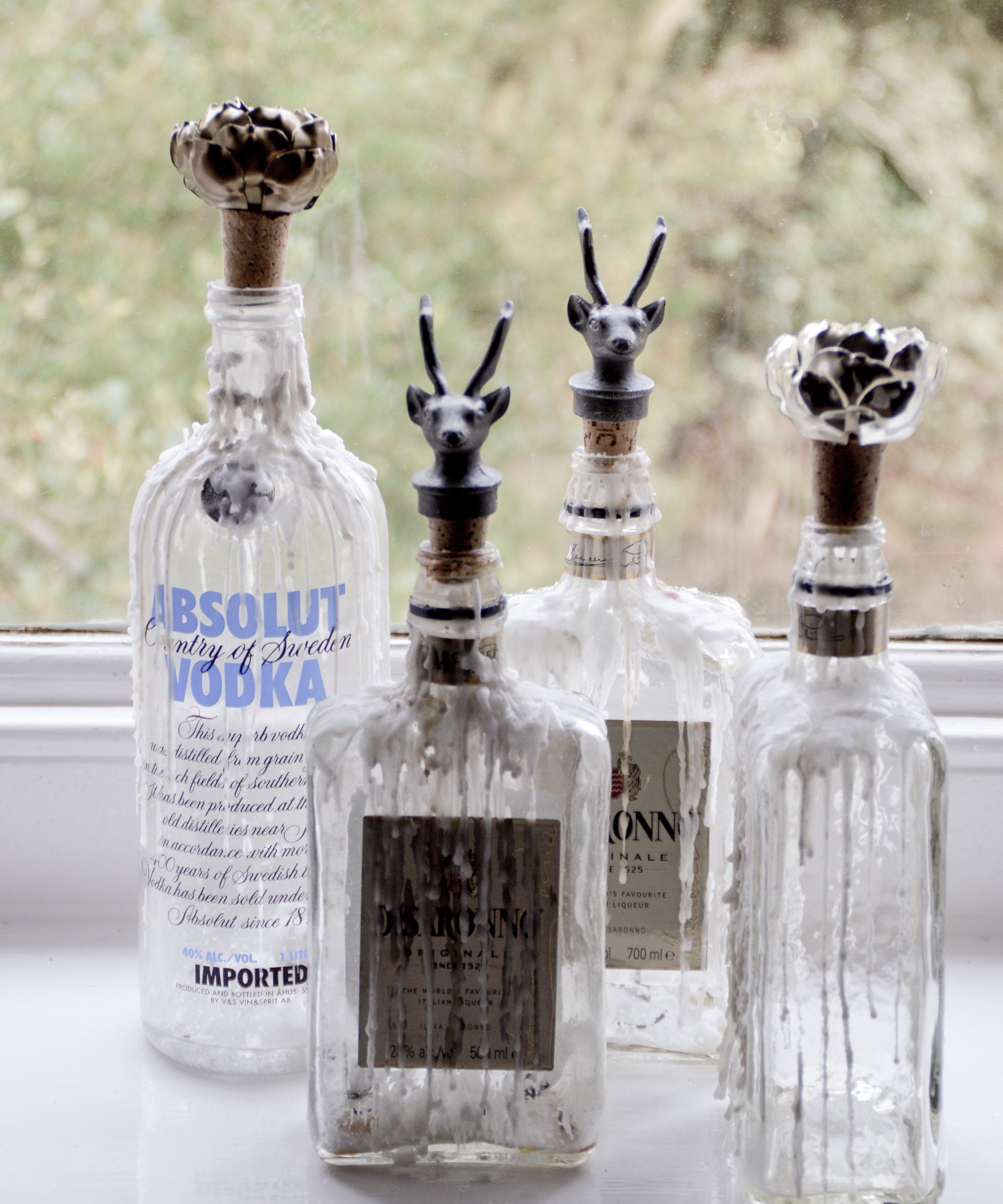 Four glass bottles with decorative animal bottle stoppers on a windowsill.
