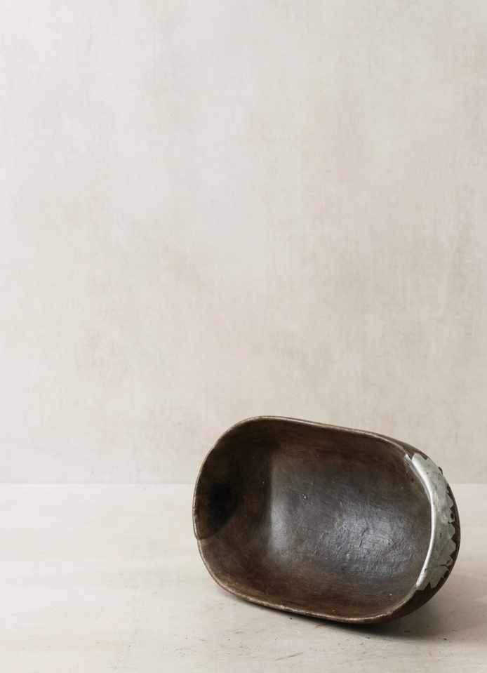 Small dark brown wooden bowl on a light beige background