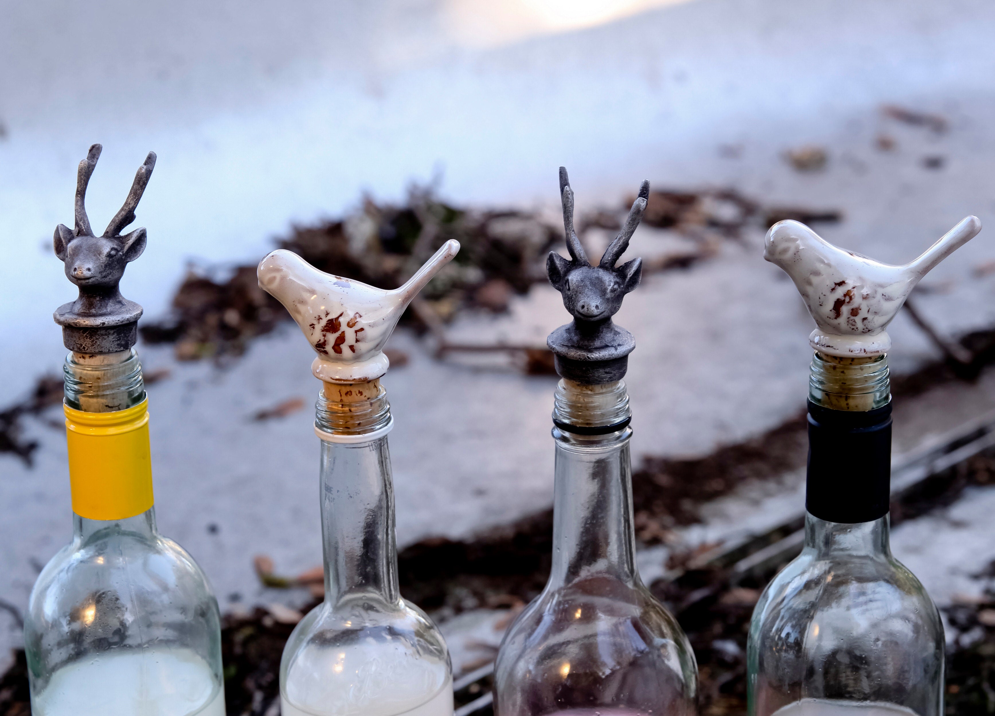 Four glass bottles with animal-shaped bottle stoppers on a rustic background