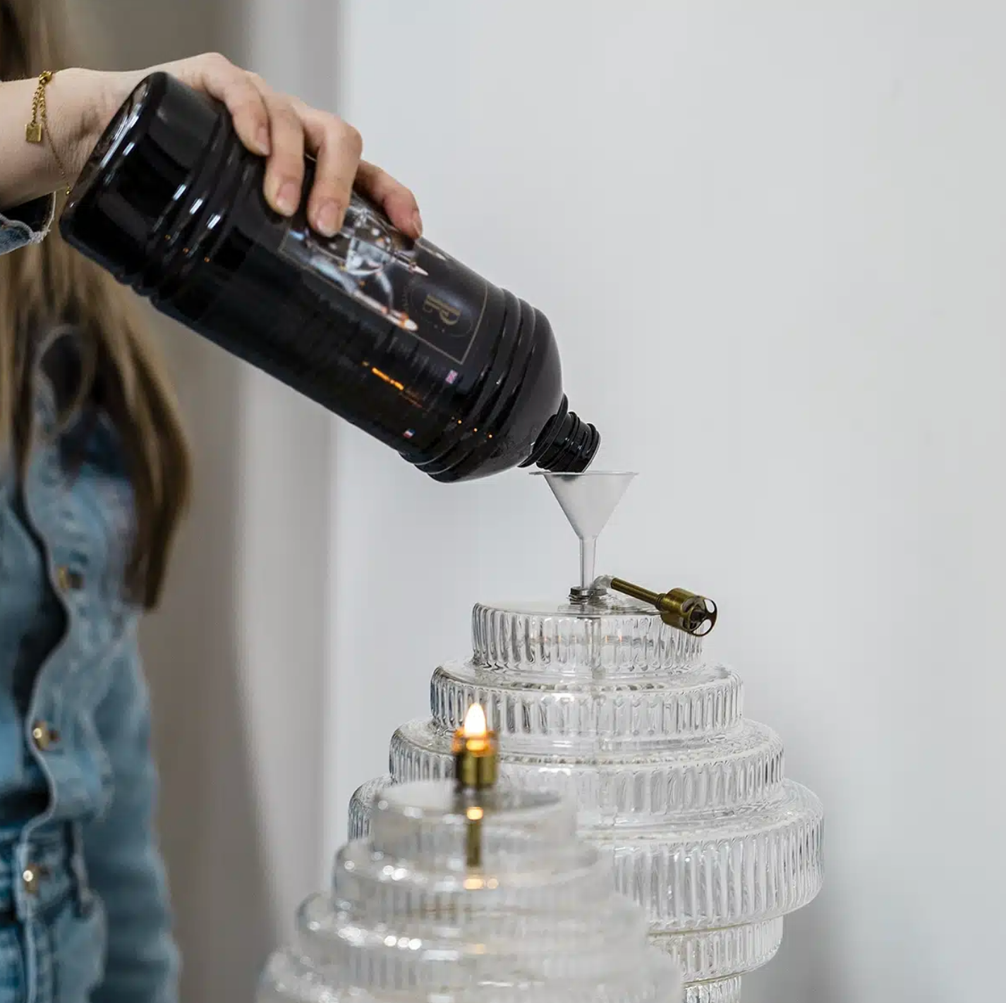 Person pouring liquid from a black bottle into a clear glass container using a funnel.