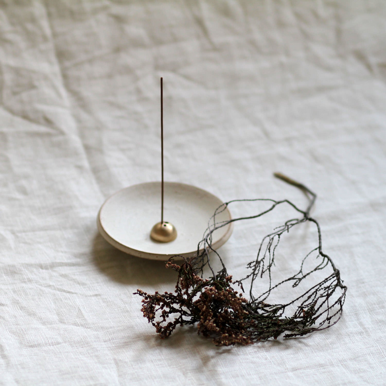 Incense stick on a small white dish with decorative wire sculpture on a textured white surface
