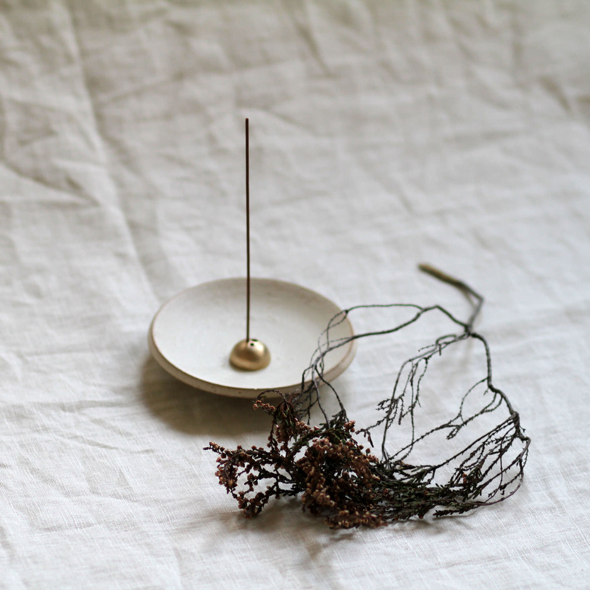 Incense stick on a small white dish with decorative wire sculpture on a textured white surface