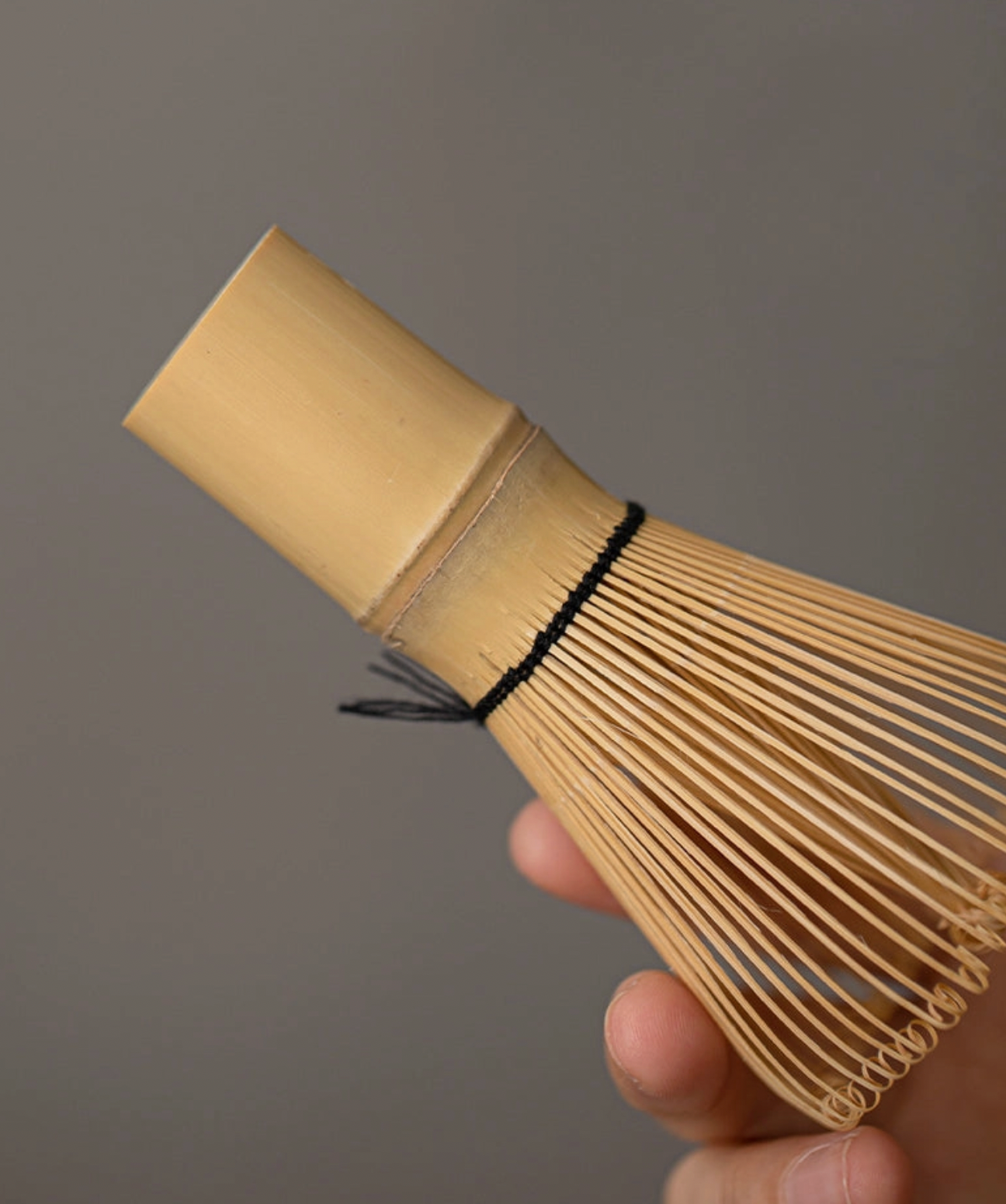 Bamboo whisk held by a hand against a gray background