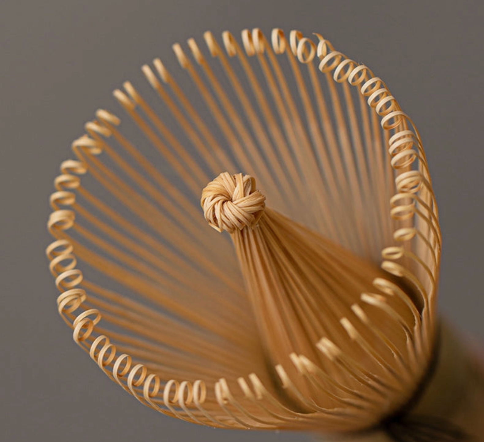 Close-up of a woven straw drink stirrer with a tassel on a dark background