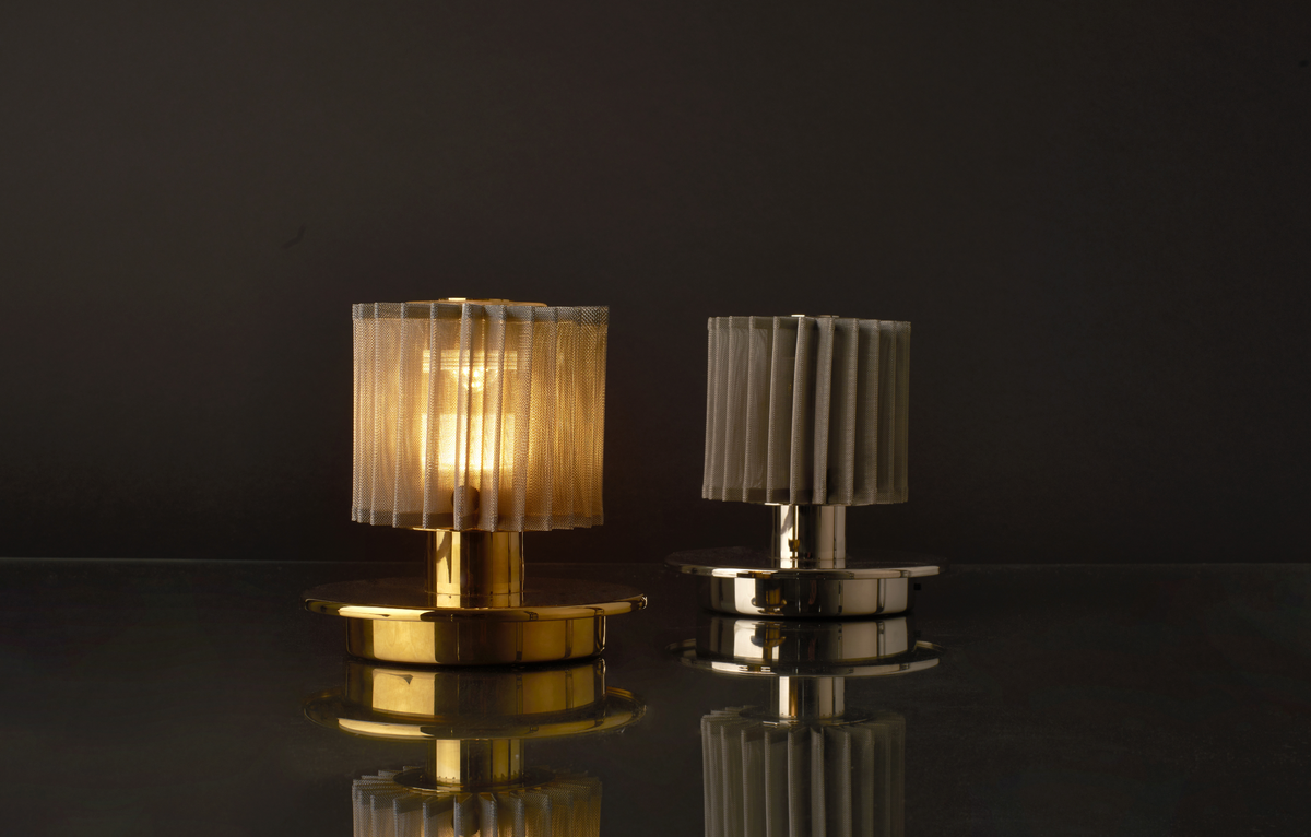 Two table lamps with pleated shades on a reflective surface with a dark background
