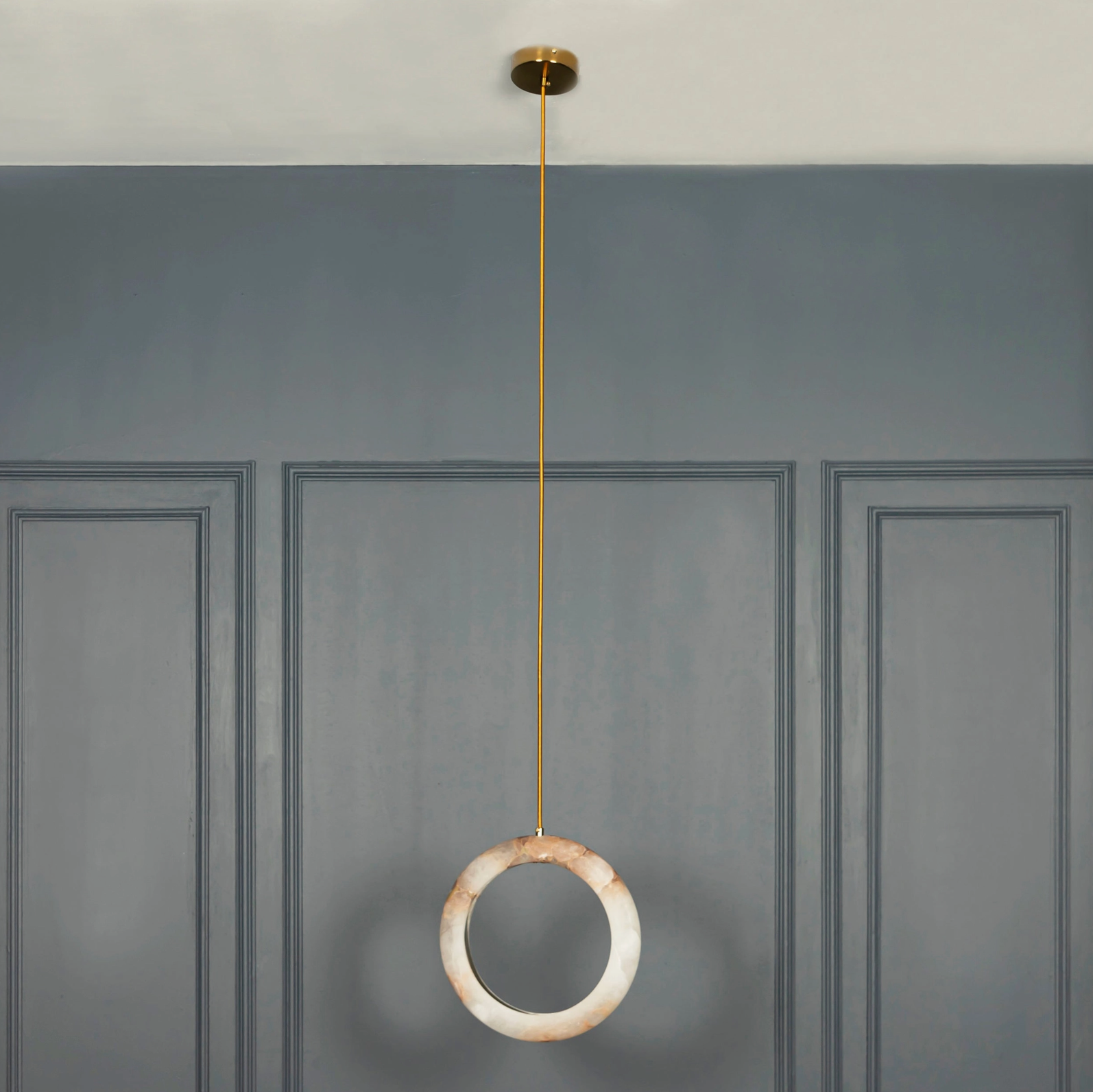 Pendant light with a circular design hanging against a gray wall.