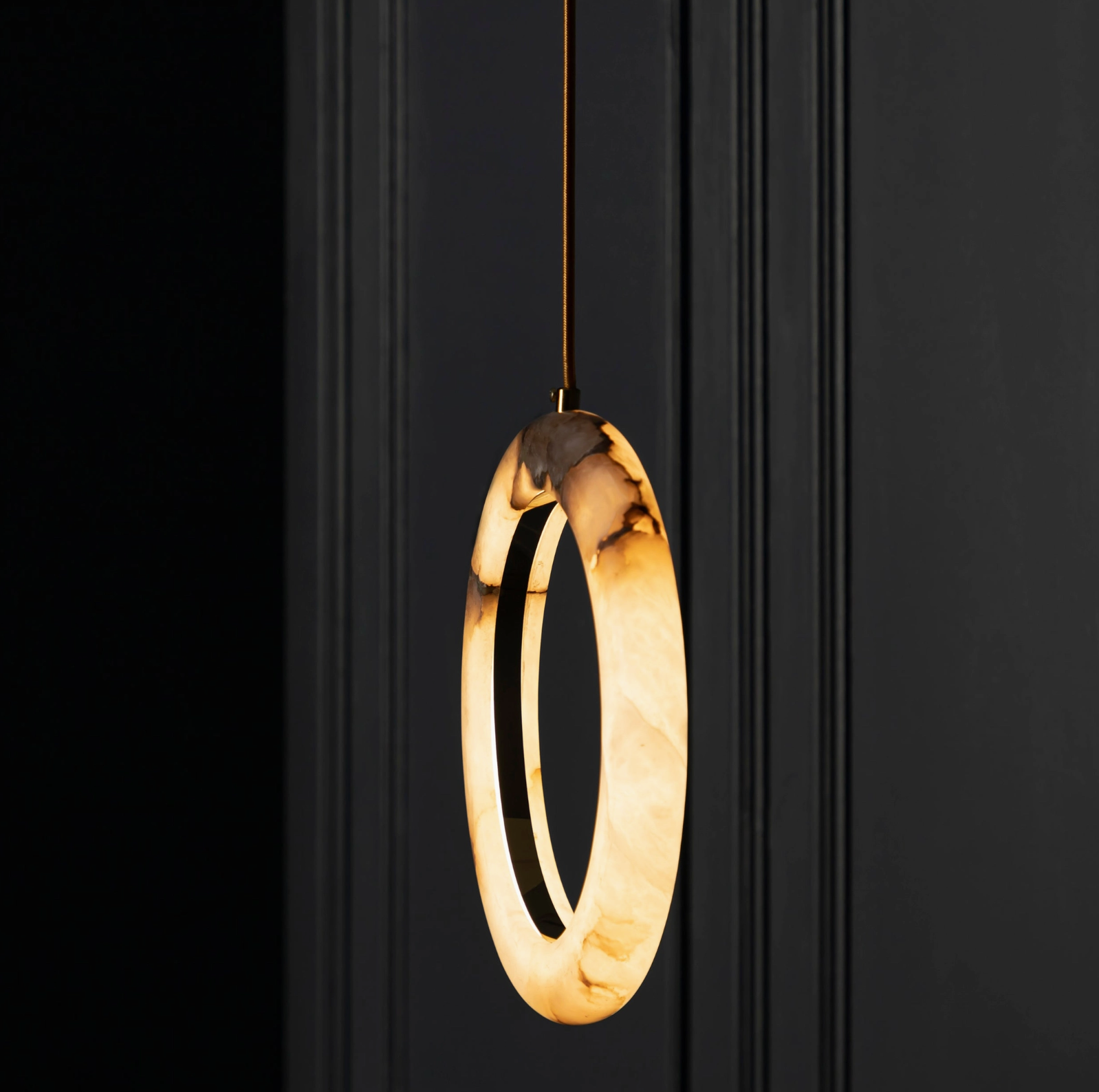 Modern pendant light with circular design hanging against a black background
