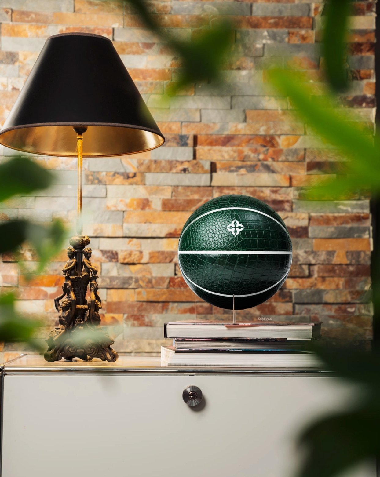 Decorative basketball on a shelf with a lamp and books against a stone wall.