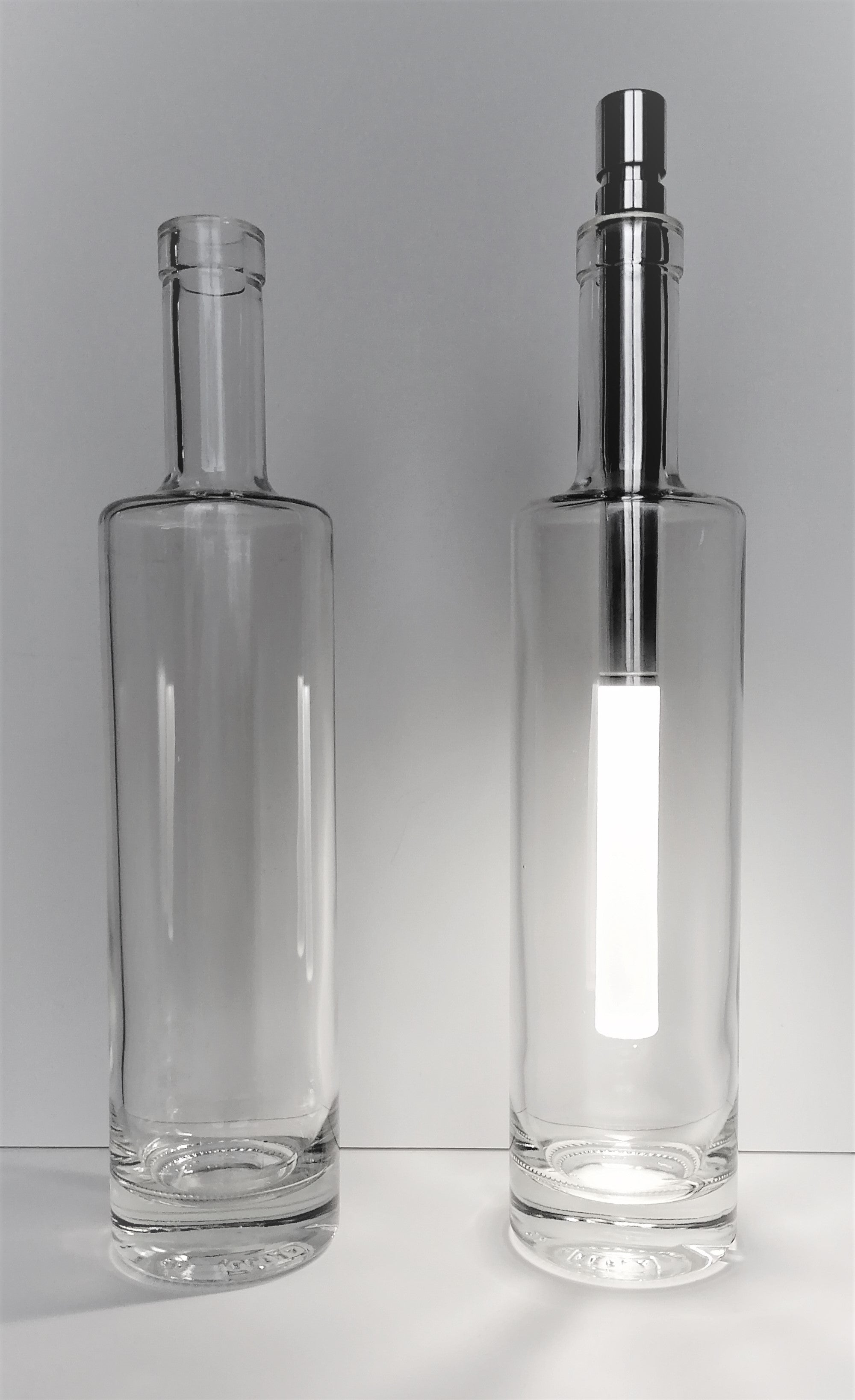 Two clear glass bottles with one having a metallic cap on a white background