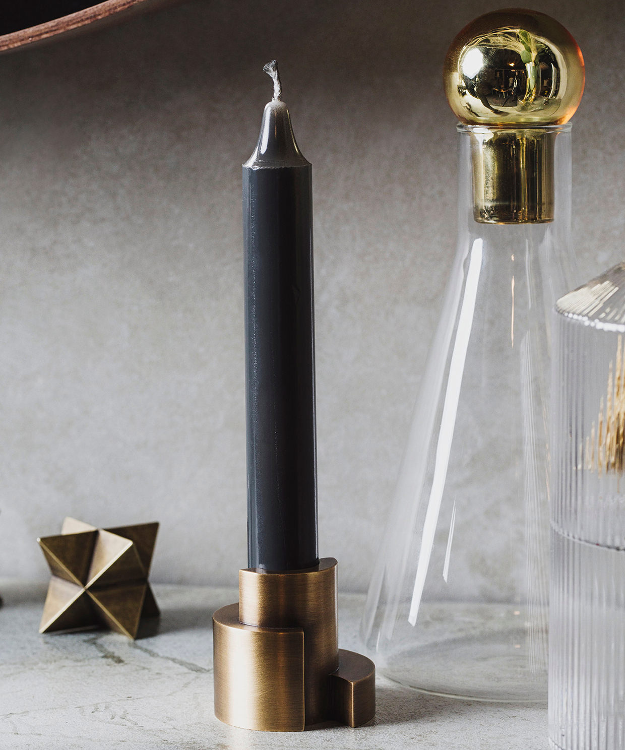 Black candle in a brass holder with a gold-topped glass bottle on a neutral background