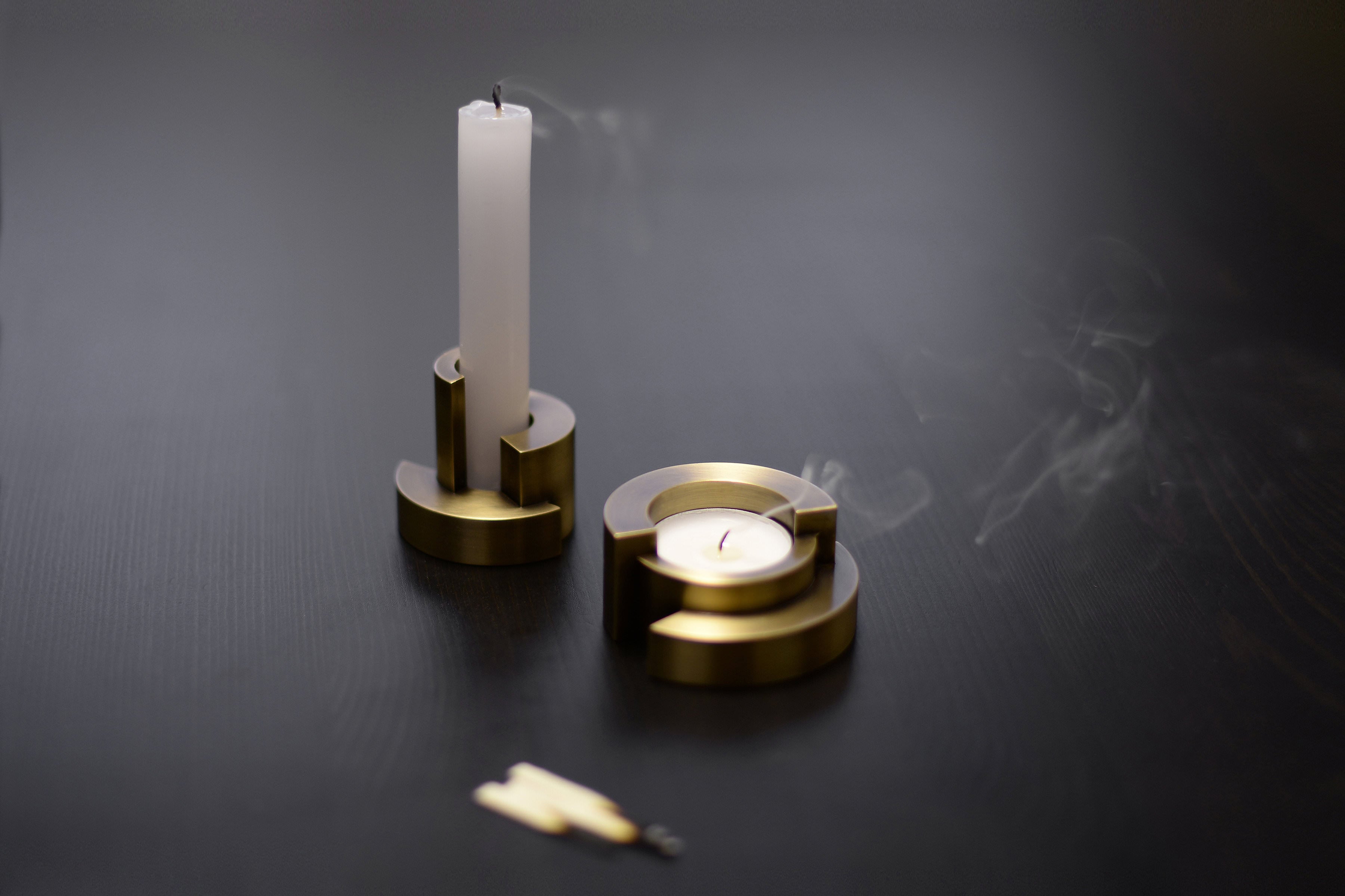 Two brass candle holders with candles on a dark surface