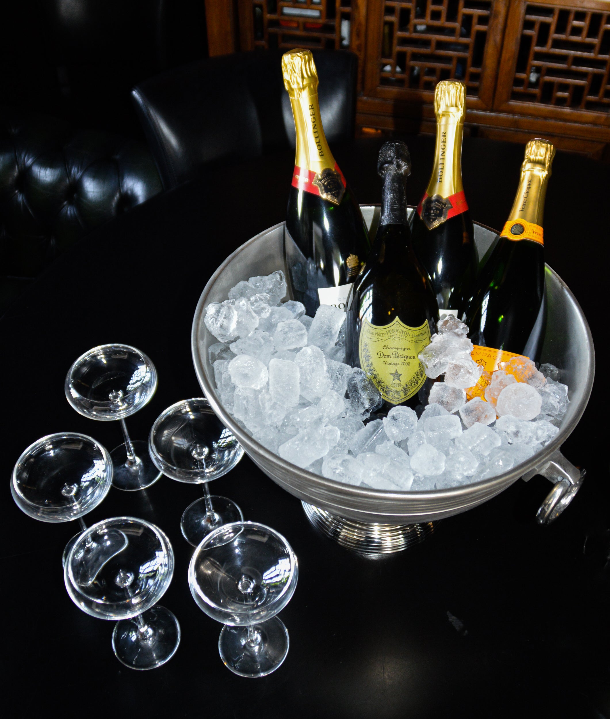 Bottles of champagne in a bucket of ice with glasses on a dark surface