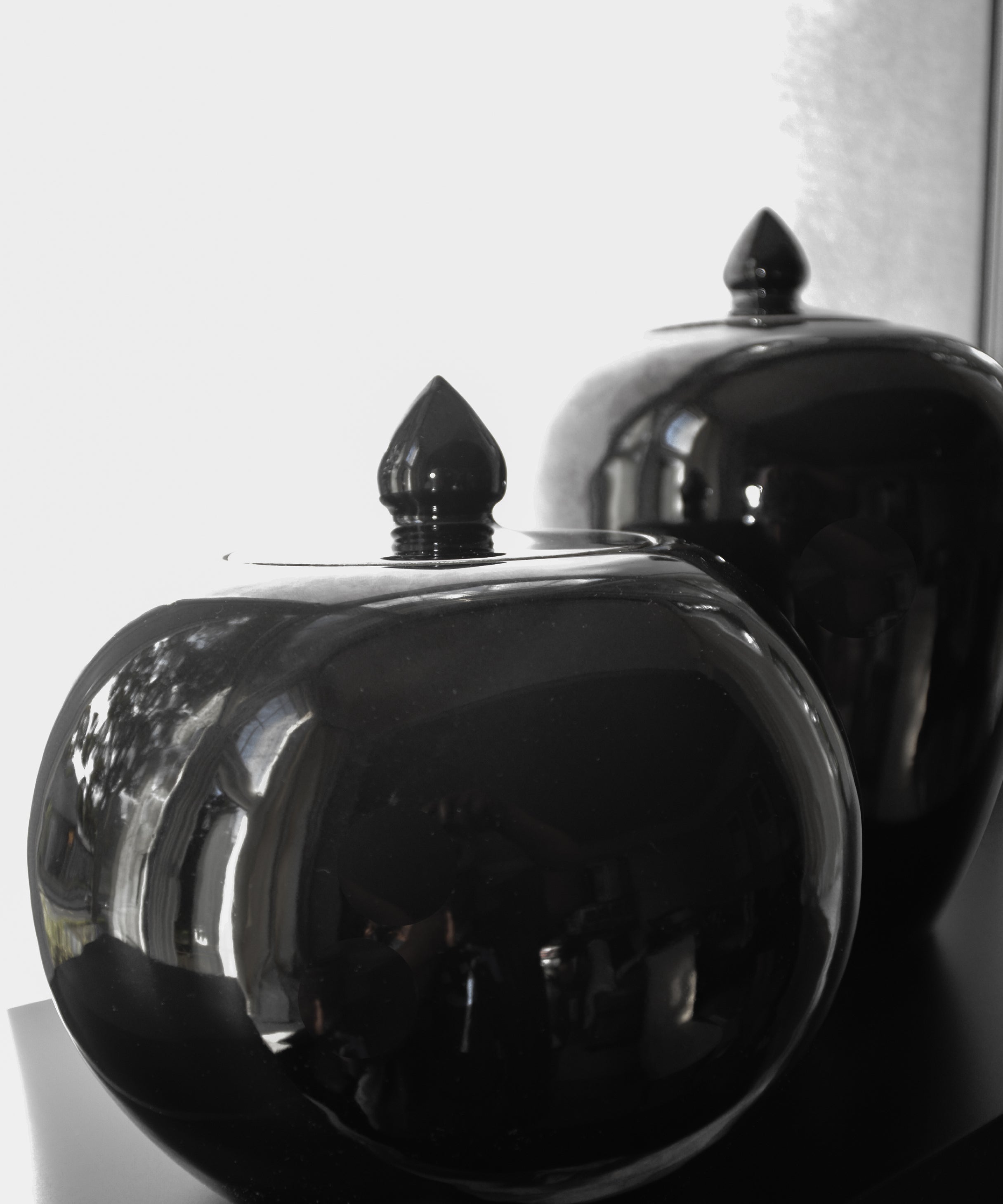 Two black ceramic jars with decorative lids on a white background