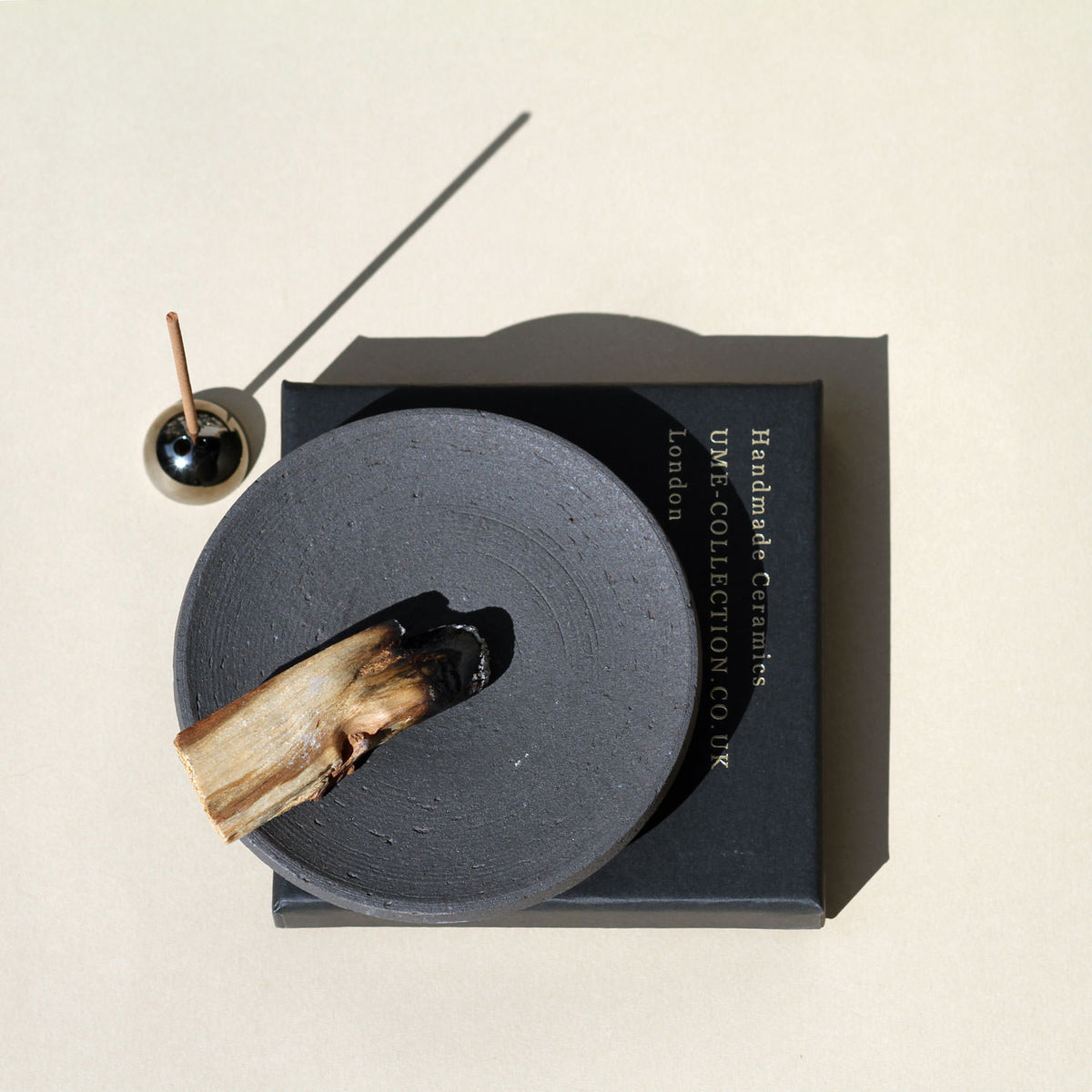 Black ceramic incense holder with a used incense stick on a beige background