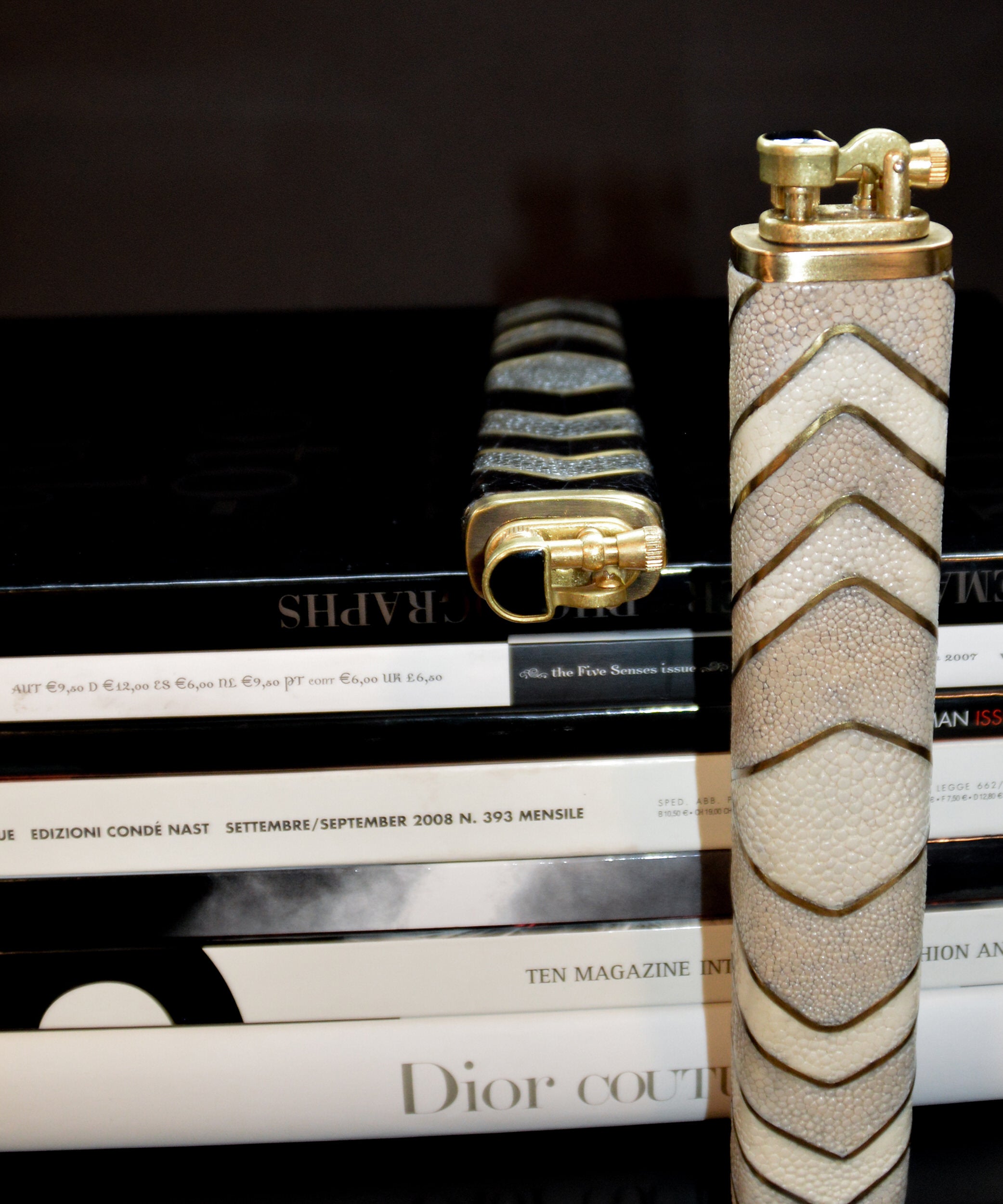 Two decorative lighters on top of a stack of magazines with visible brand names.