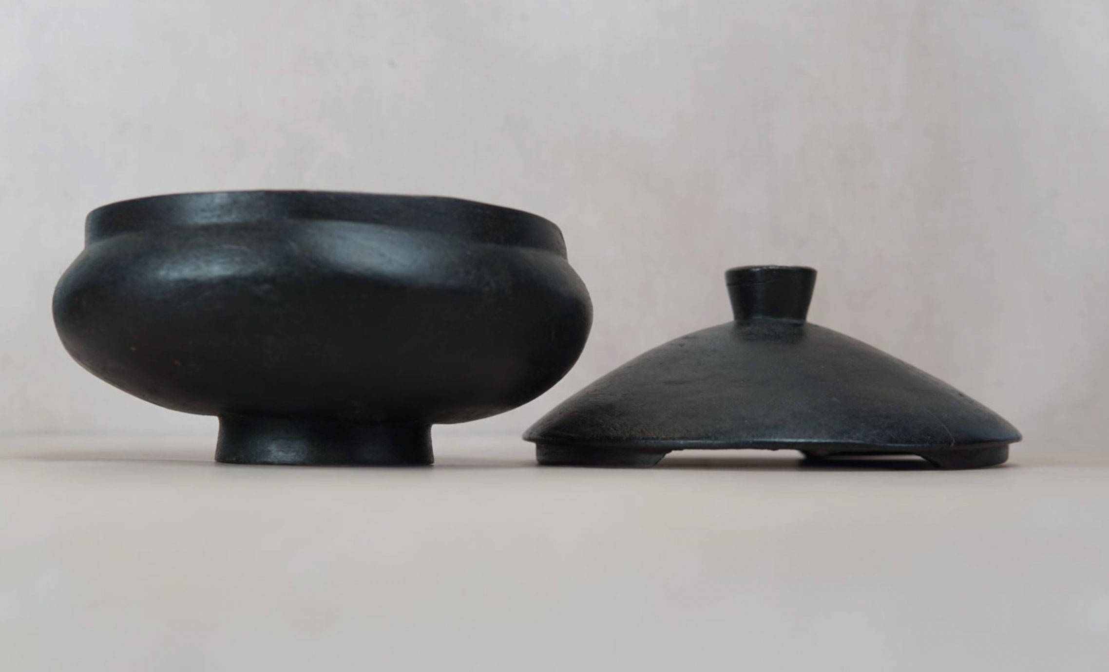 Two black ceramic bowls with lids on a light gray background