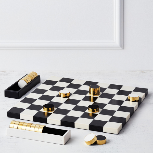 Checkers game set with black and white board and gold pieces on a light gray surface.