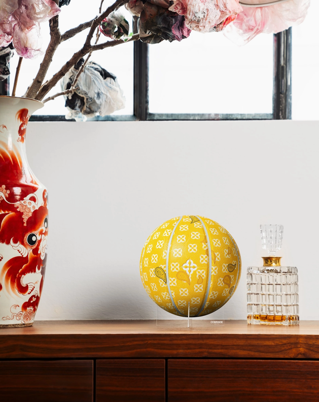 Decorative yellow sphere with a pattern on a wooden surface next to a floral arrangement and a vase.