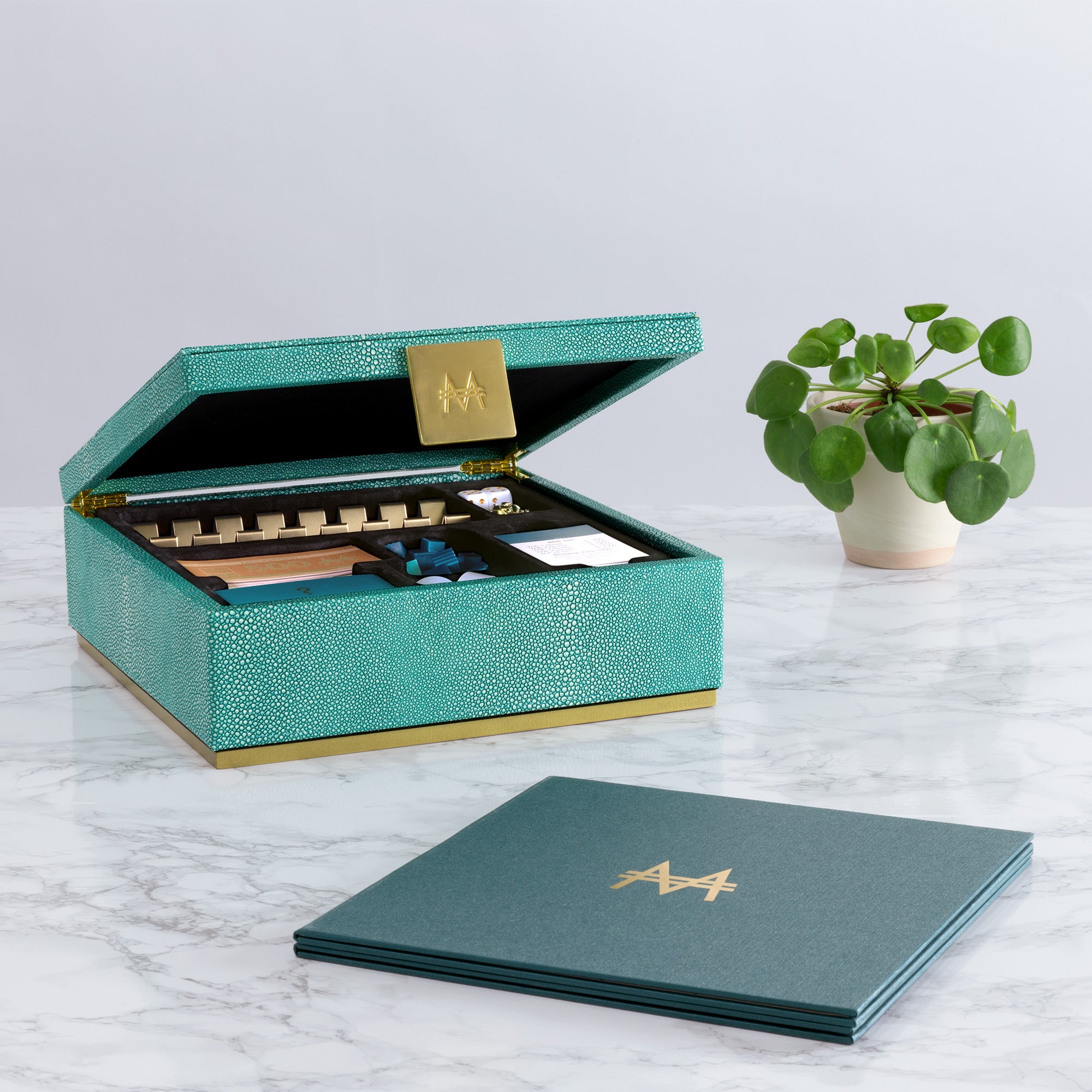 Teal jewelry box with gold accents on a marble surface with a plant in the background