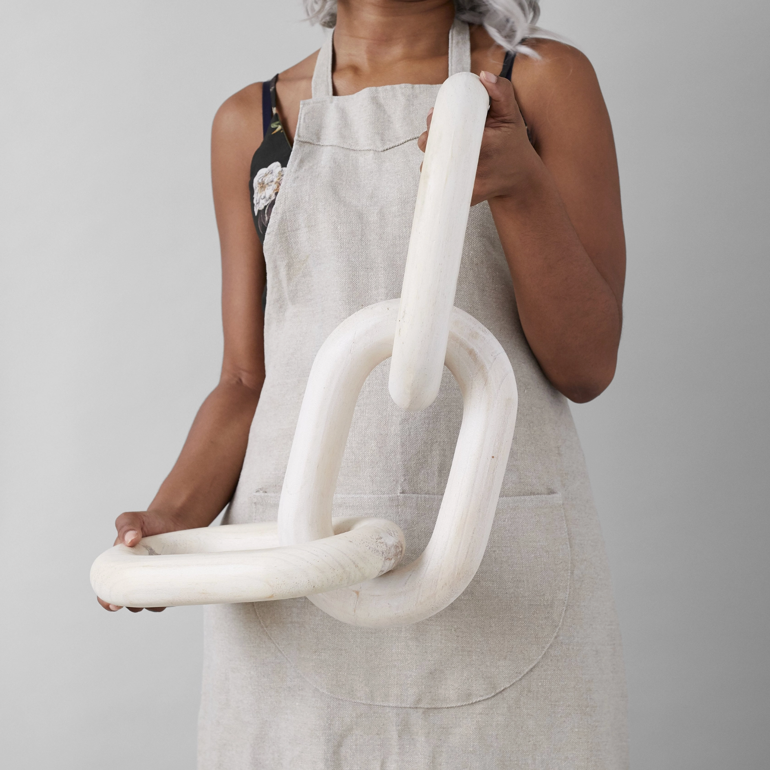 Person wearing a light apron holding a white ceramic sculpture against a plain background