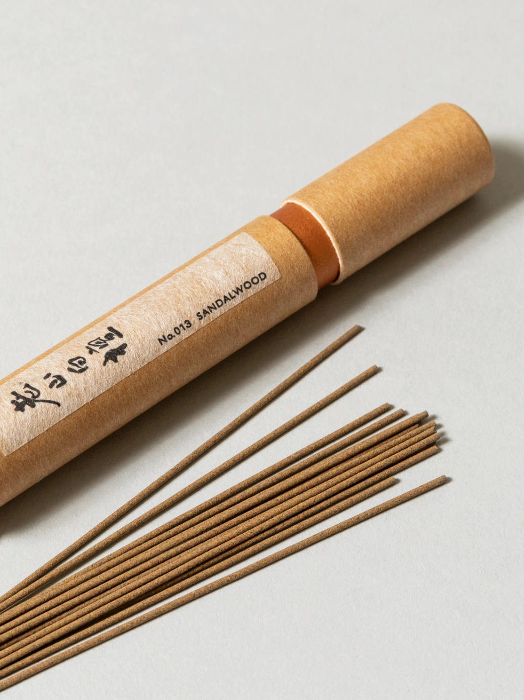 Sandalwood incense sticks with a cardboard tube on a light gray background