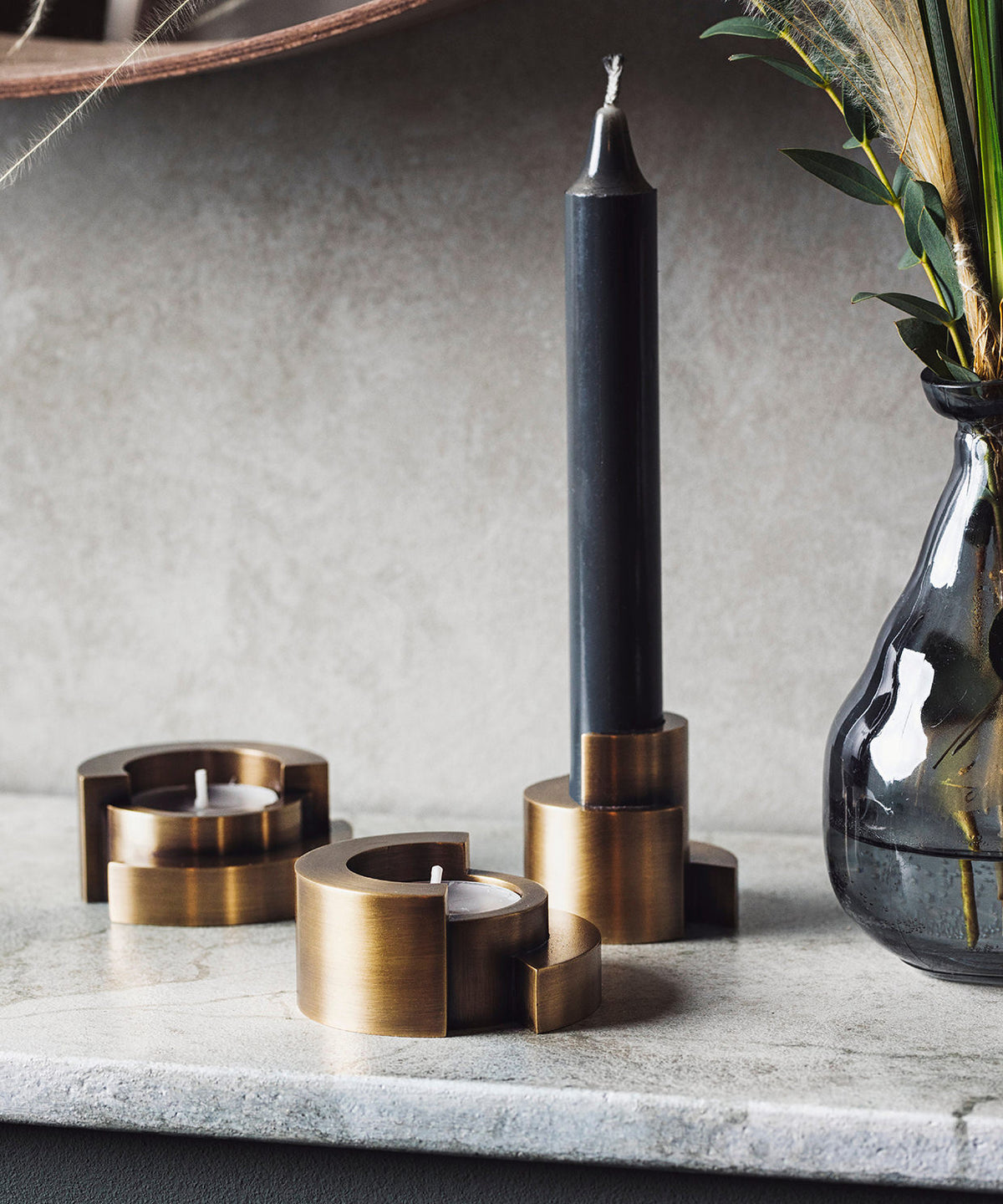 Decorative candle holders and a black candle on a marble surface with a vase in the background.