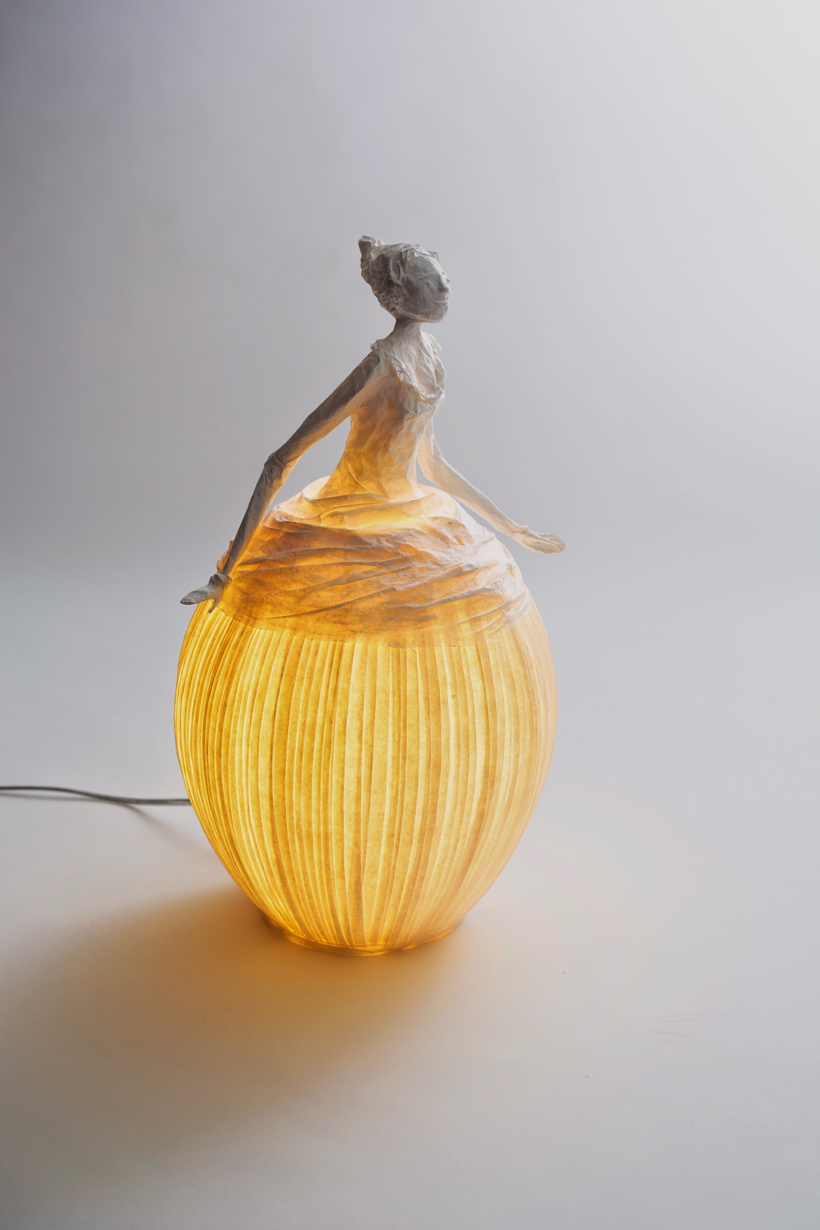 Decorative lamp with a figurine on top, emitting a warm glow against a plain background