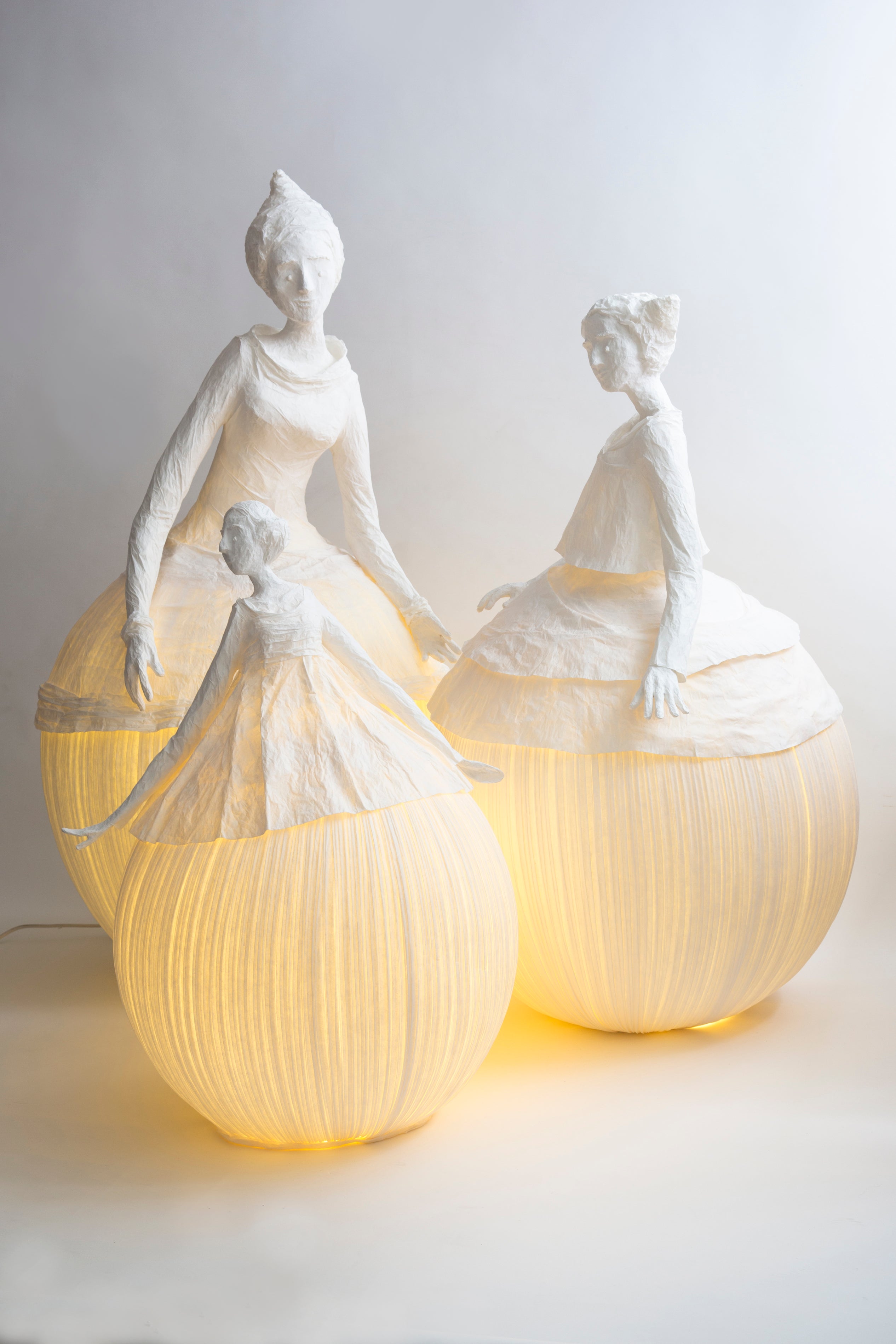 Two illuminated paper sculptures of women on a white background