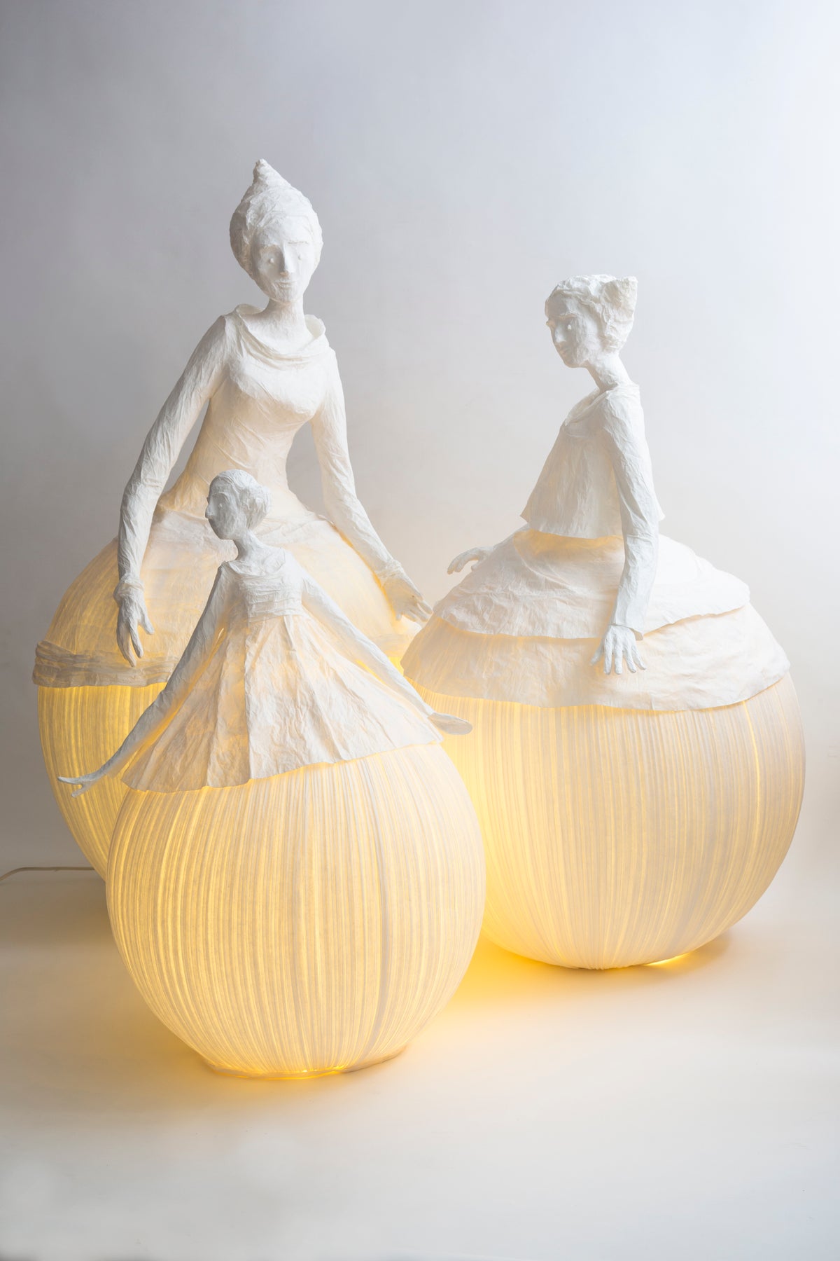 Two illuminated paper sculptures of women on a white background