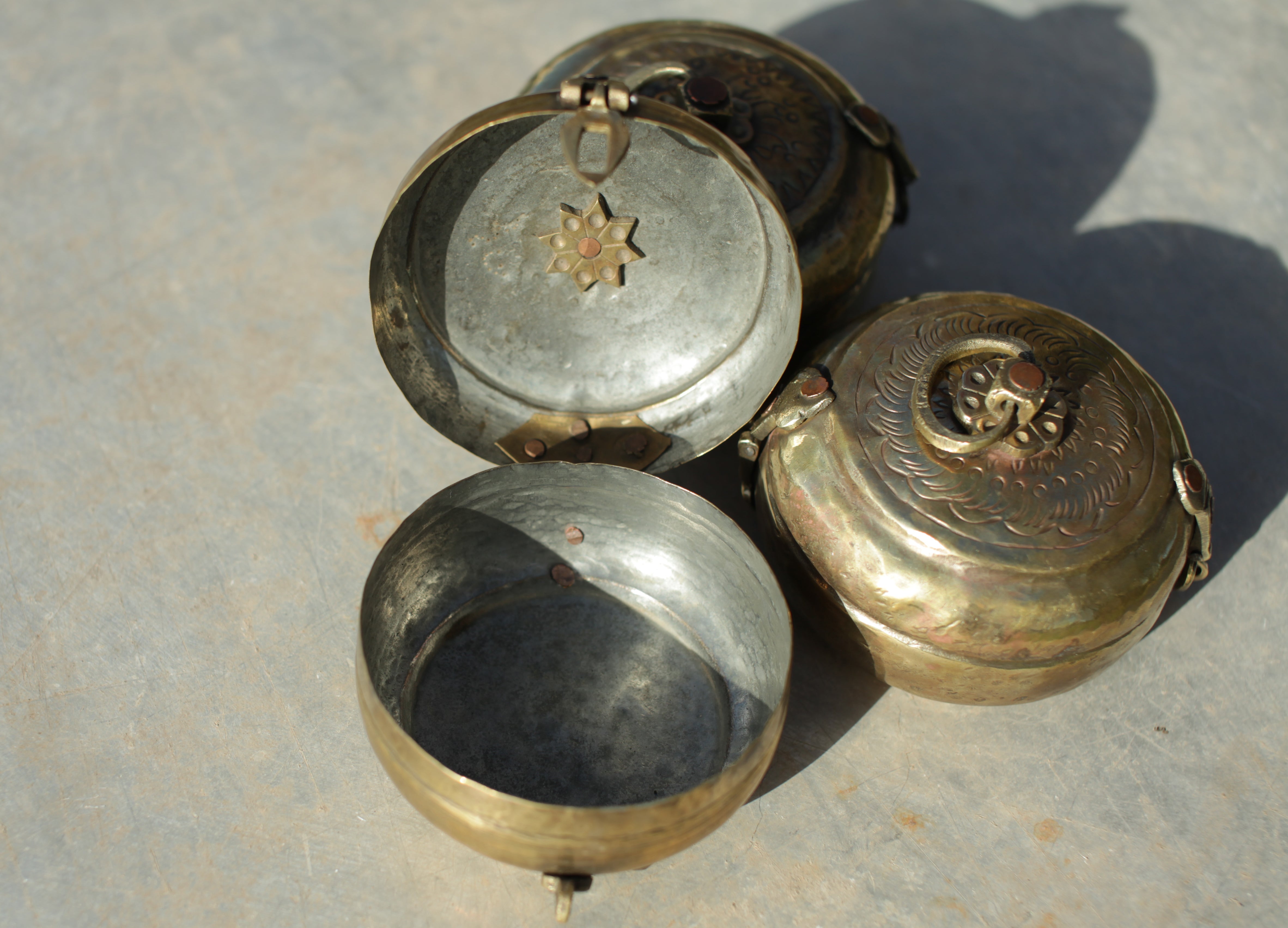 Three vintage metal containers with intricate designs on a textured surface