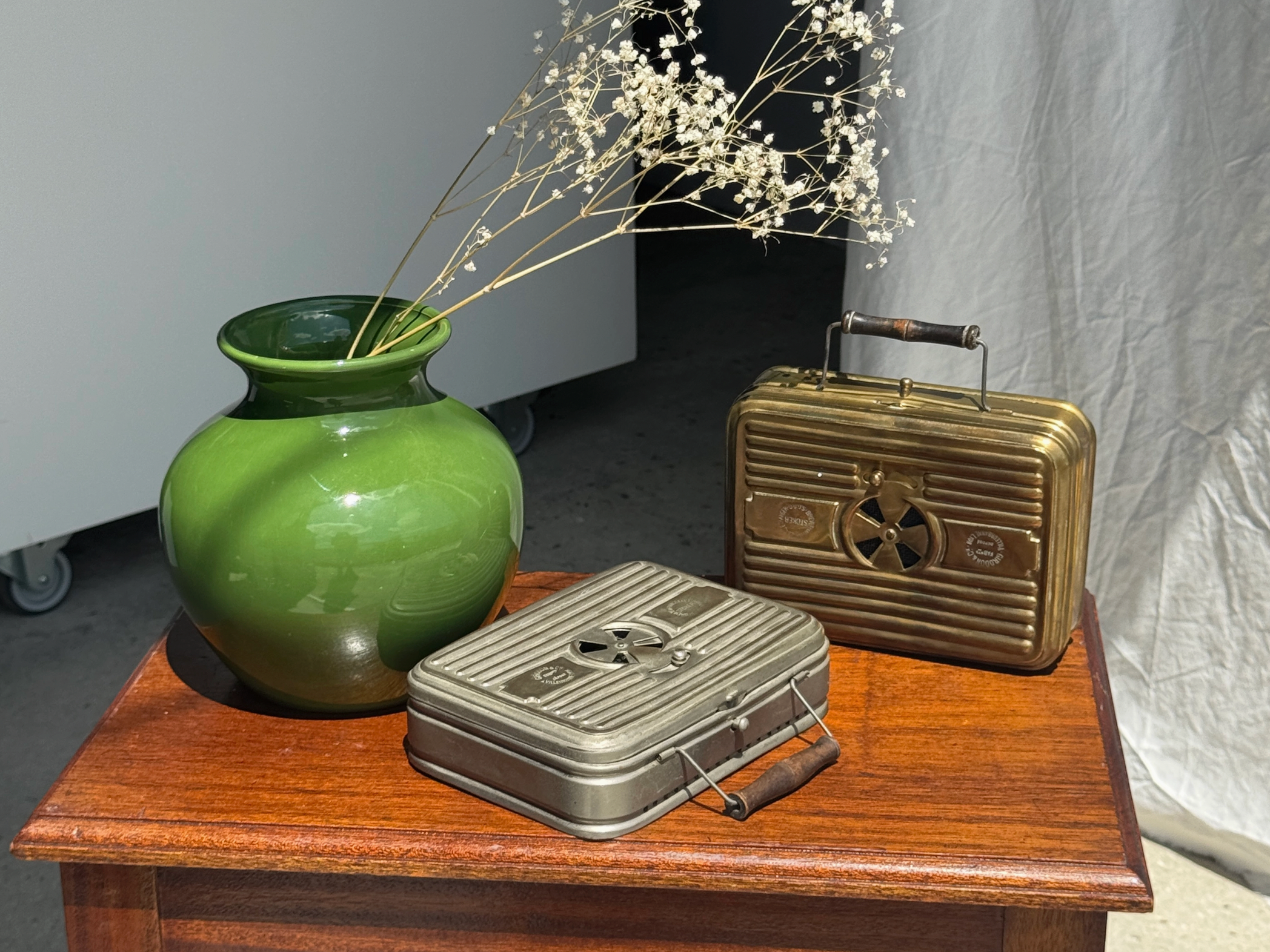 Green vase with dried plants on a wooden table next to vintage-style suitcases.