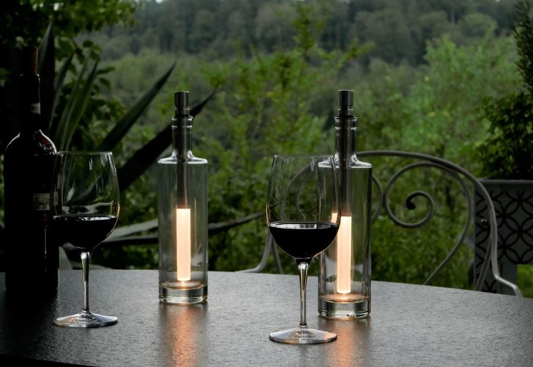 Two wine glasses with red wine and two glass bottles with candles on a table outdoors.