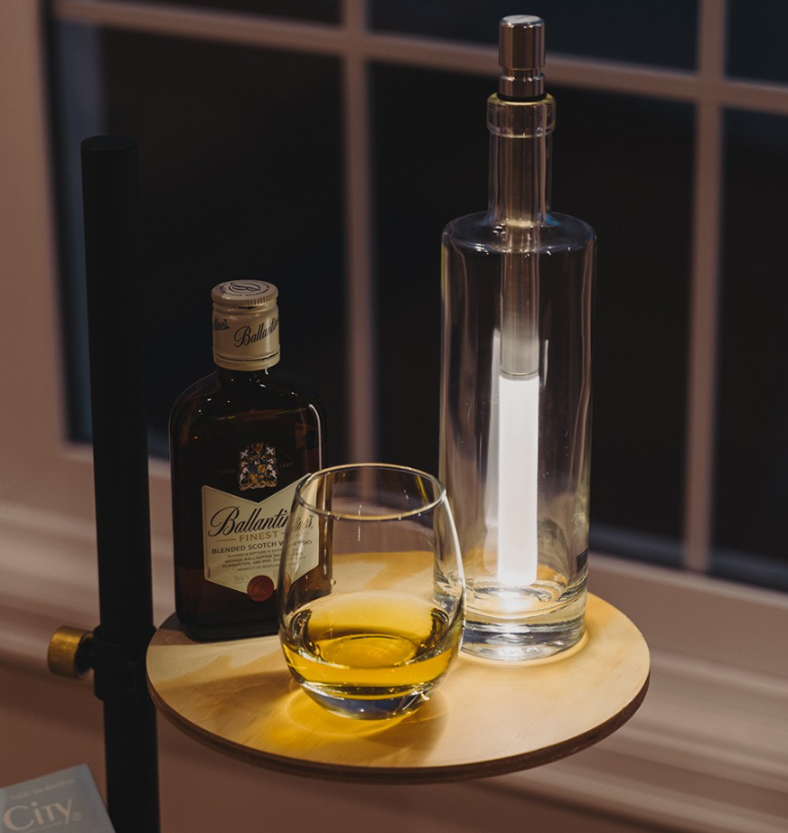 Bottle of Ballantine's whisky, glass with whisky, and decanter on a wooden tray.