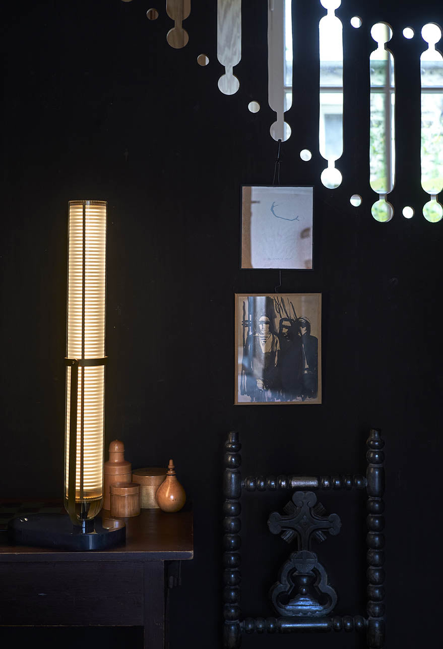 Dark room with a tall lamp, wooden chair, and framed pictures on a dark wall.