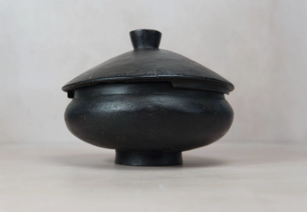 Black ceramic pot with lid on a light gray background