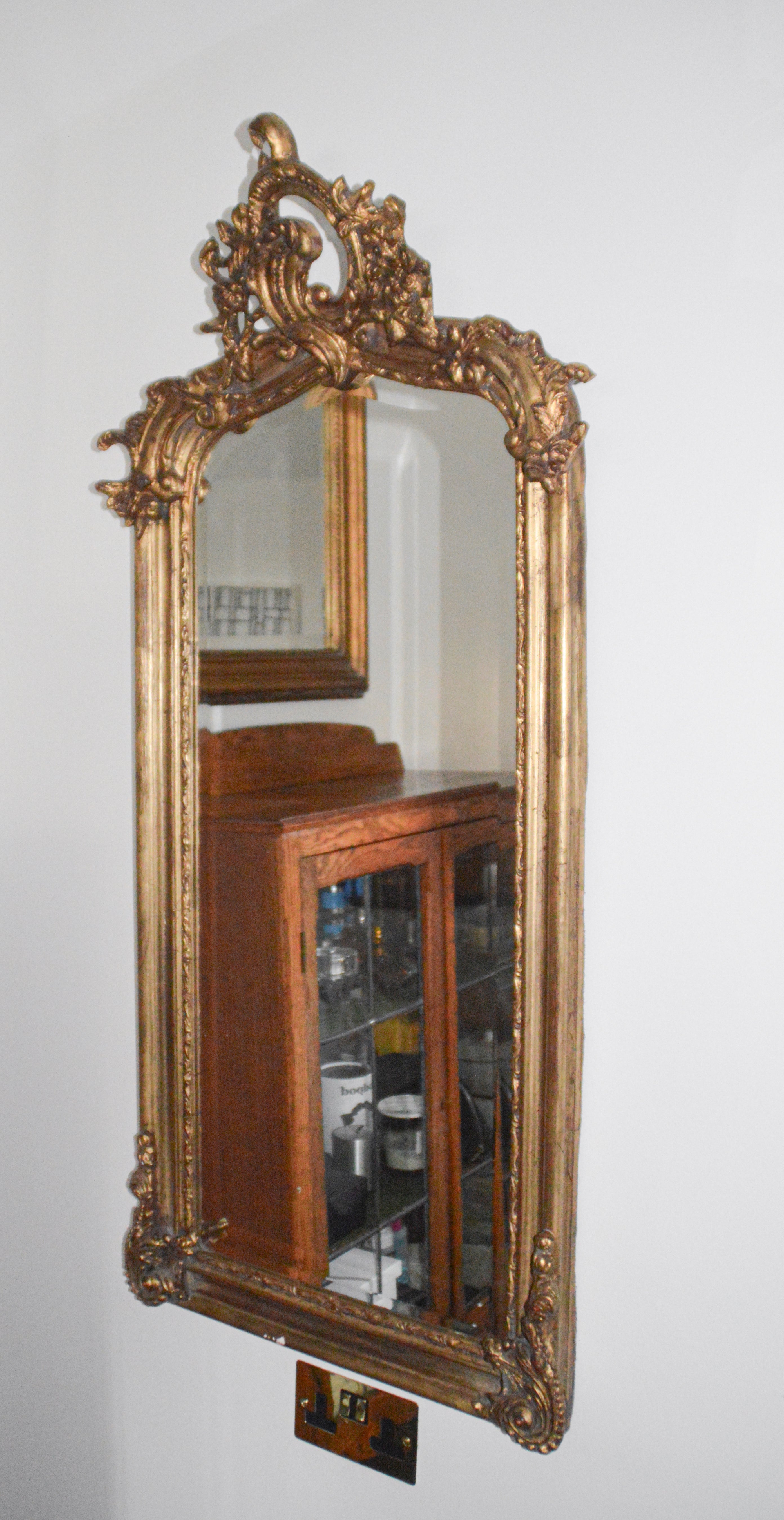 Decorative gold-framed mirror on a white wall