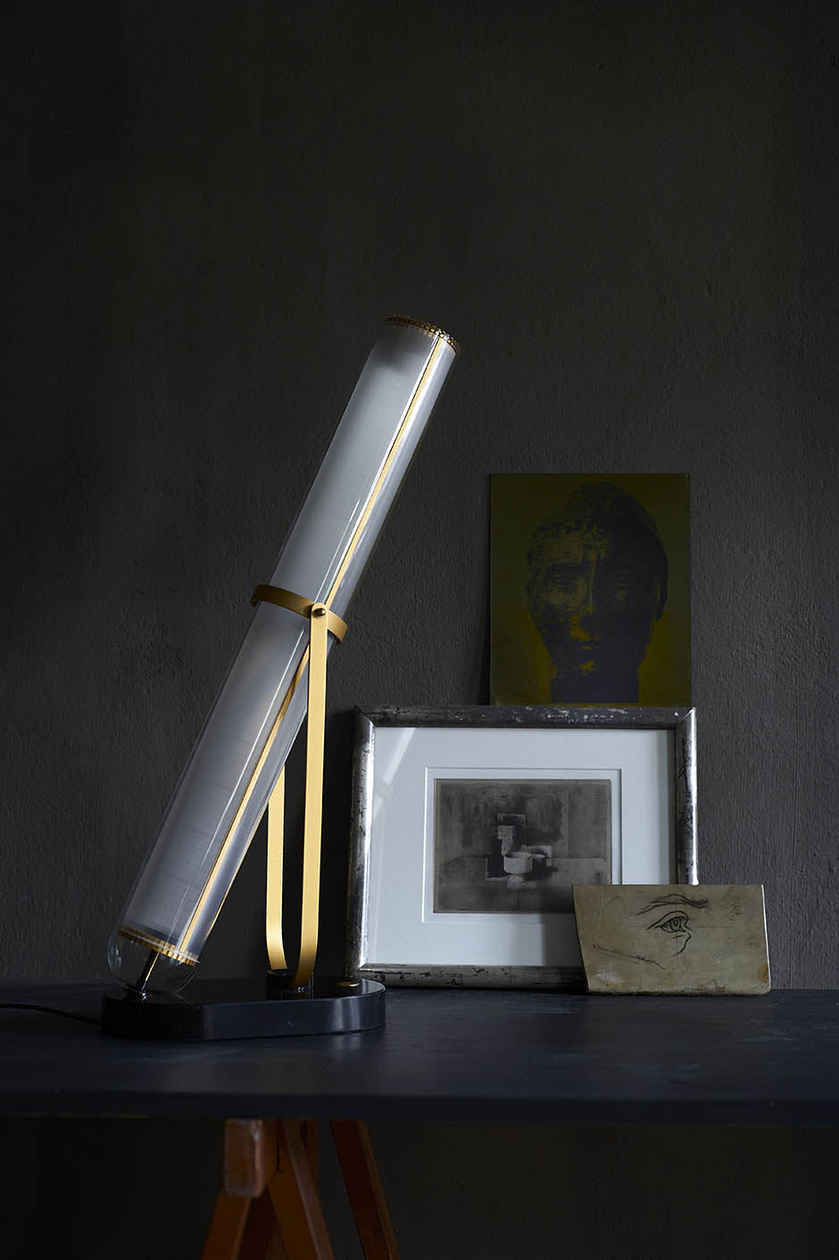 Modern desk lamp on a dark surface with framed pictures in the background