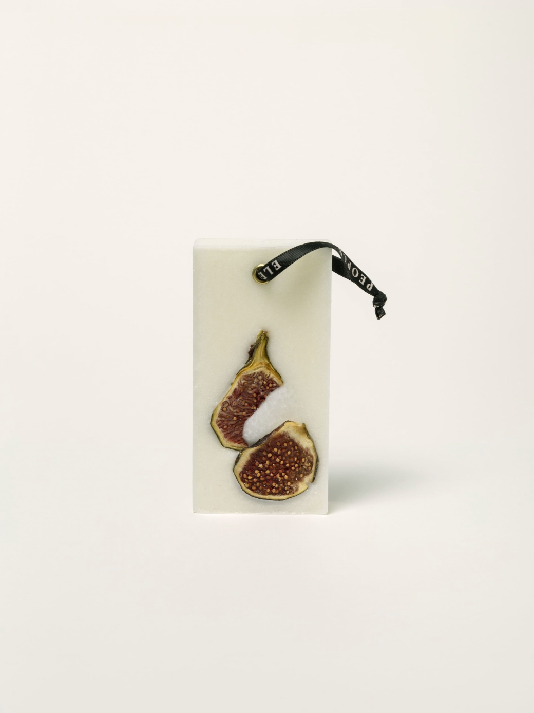 Fig-shaped earrings on a white card with a black strap, on a light beige background