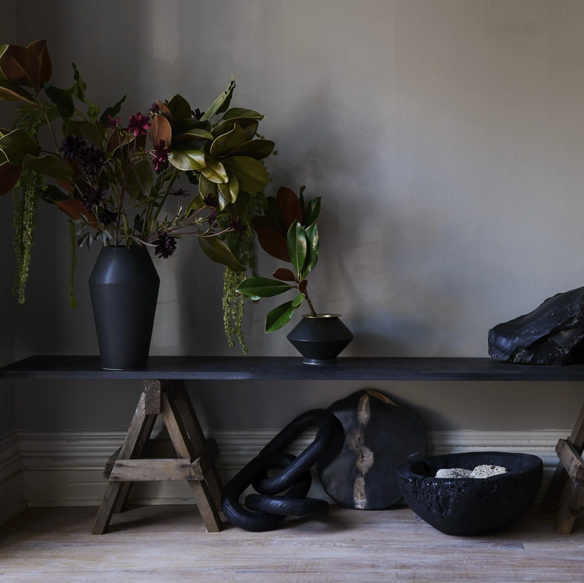 Decorative setting with vases, plants, and stones against a neutral wall.