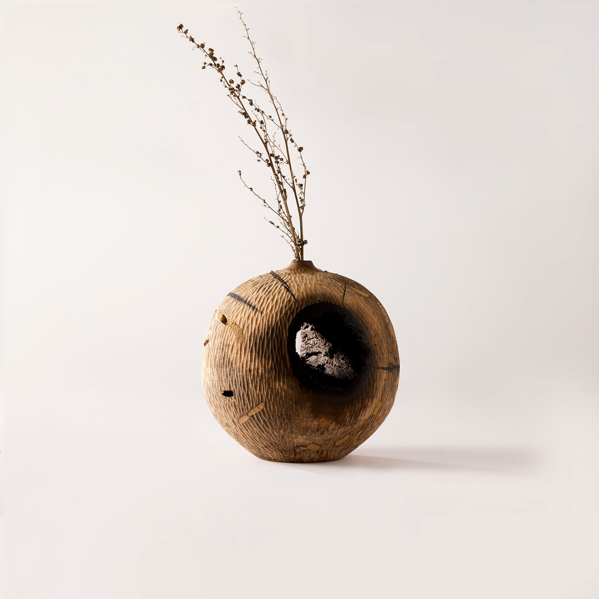 Wooden vase with a natural finish and dried branches on a light background