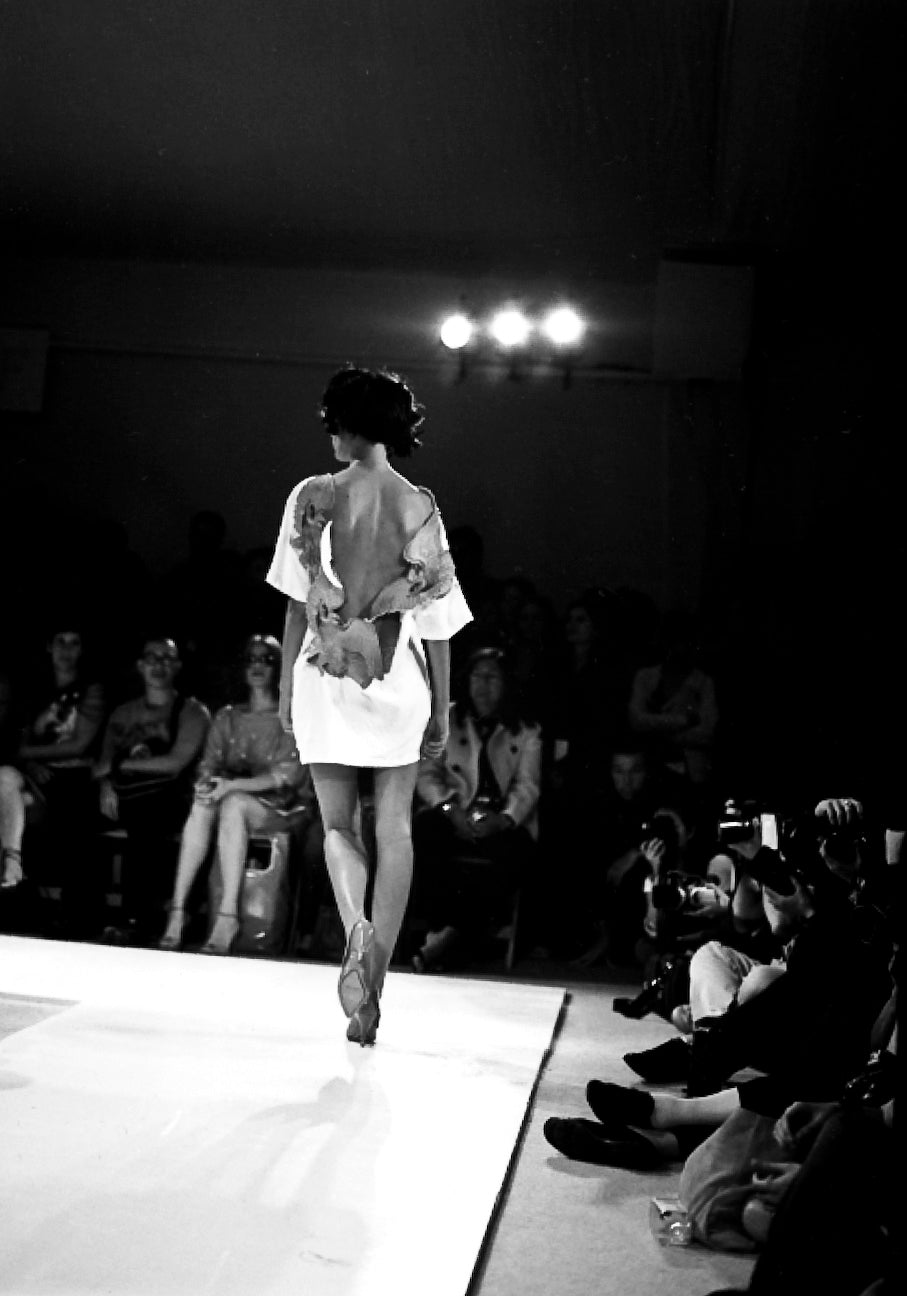 Model walking on a fashion show runway with an audience watching.