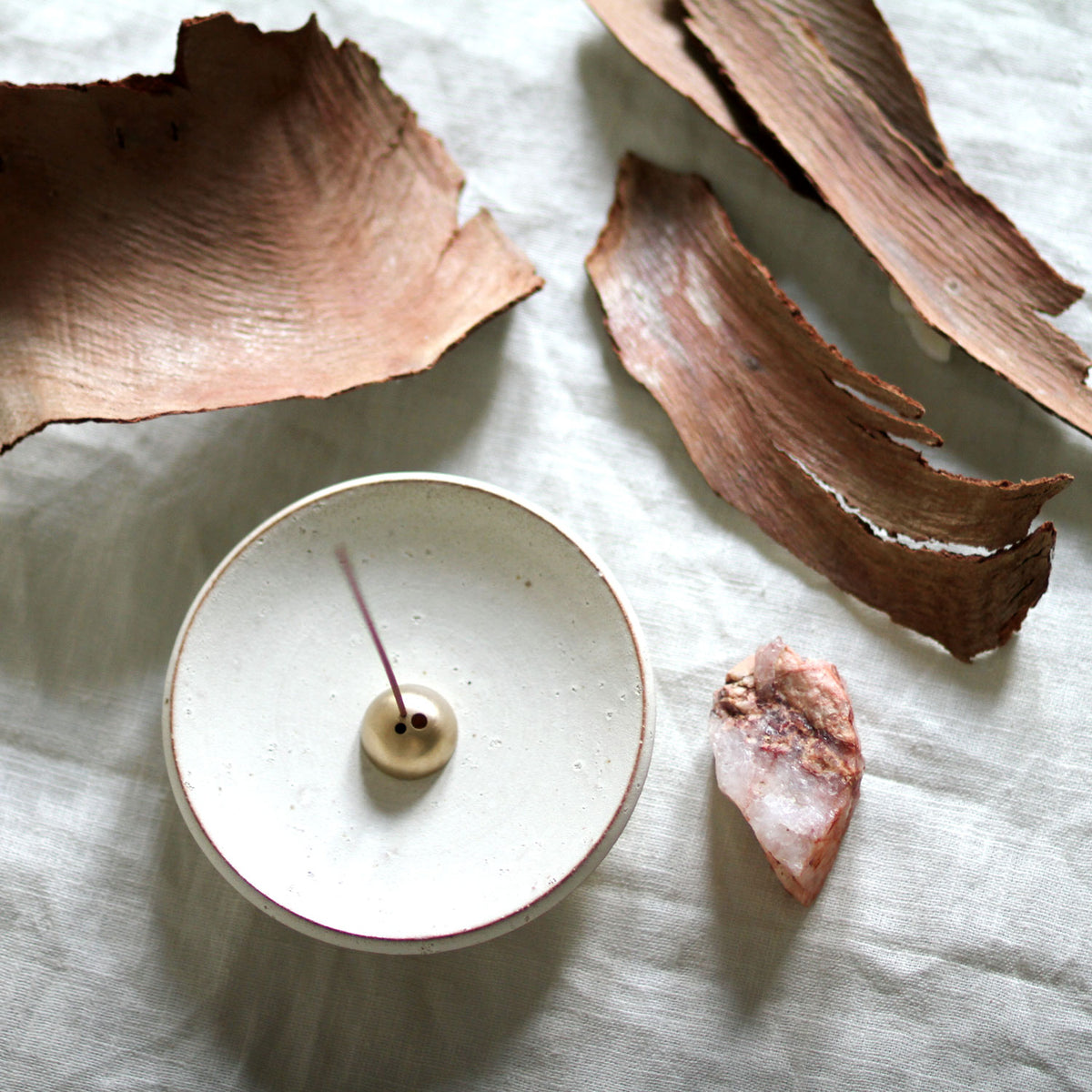 Incense burner with a stick on a light surface with dried leaves and a crystal.