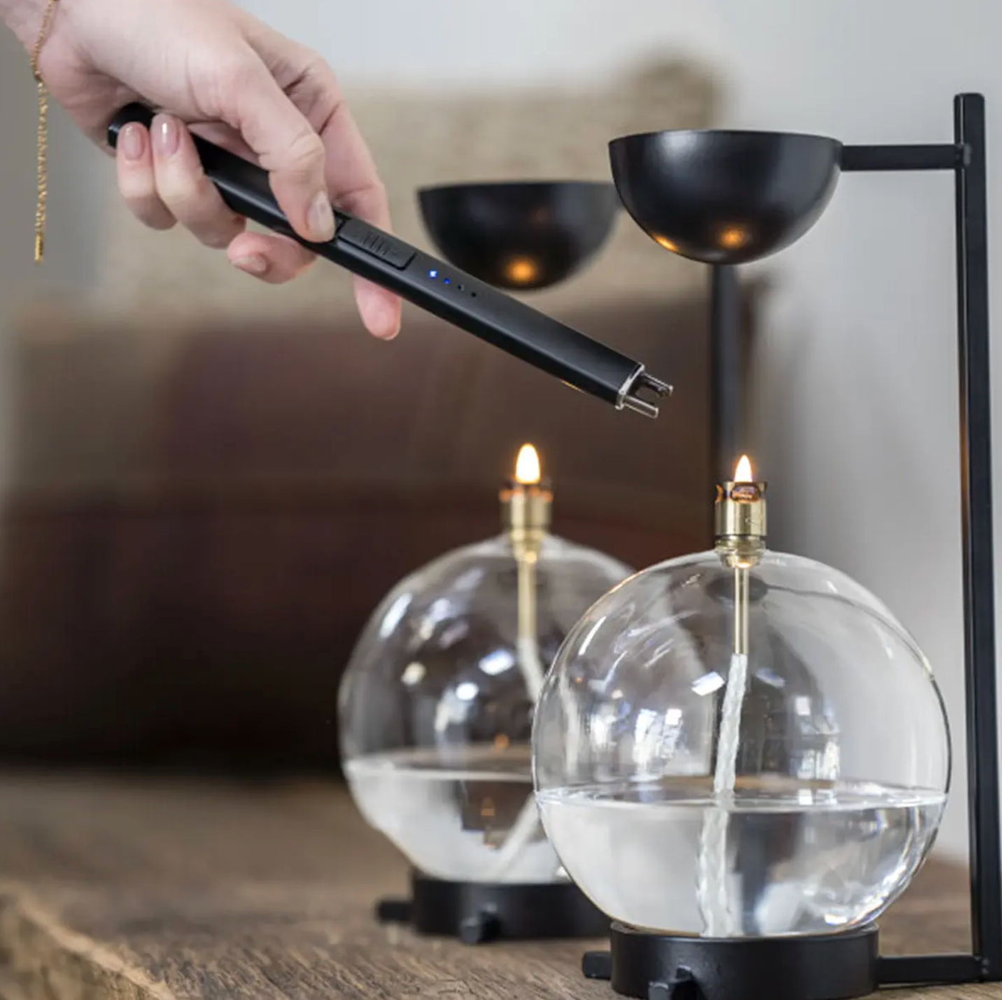 Person using a lighter to light a candle inside a glass container with a blurred background