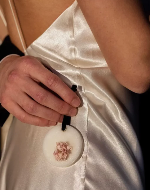 Close-up of a hand holding a white scented was bar with floral design against a white fabric background