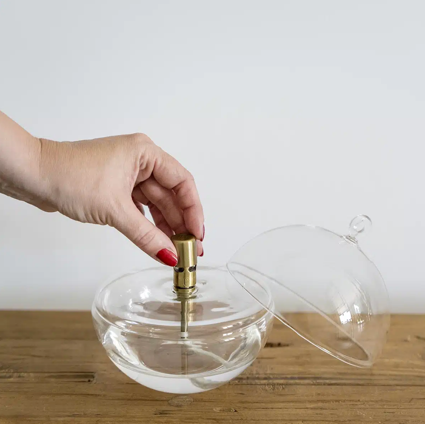 Hand holding a clear glass container with a gold cap on a wooden surface.